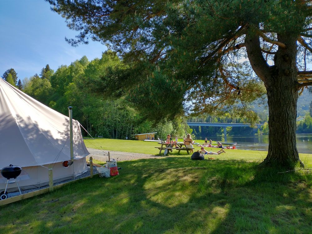 gjester koser seg på plenen ved vannet på Lystang Glamping i Notodden