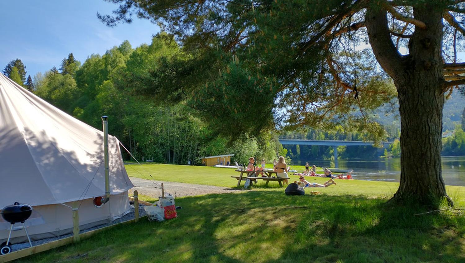 gjester koser seg på plenen ved vannet på Lystang Glamping i Notodden