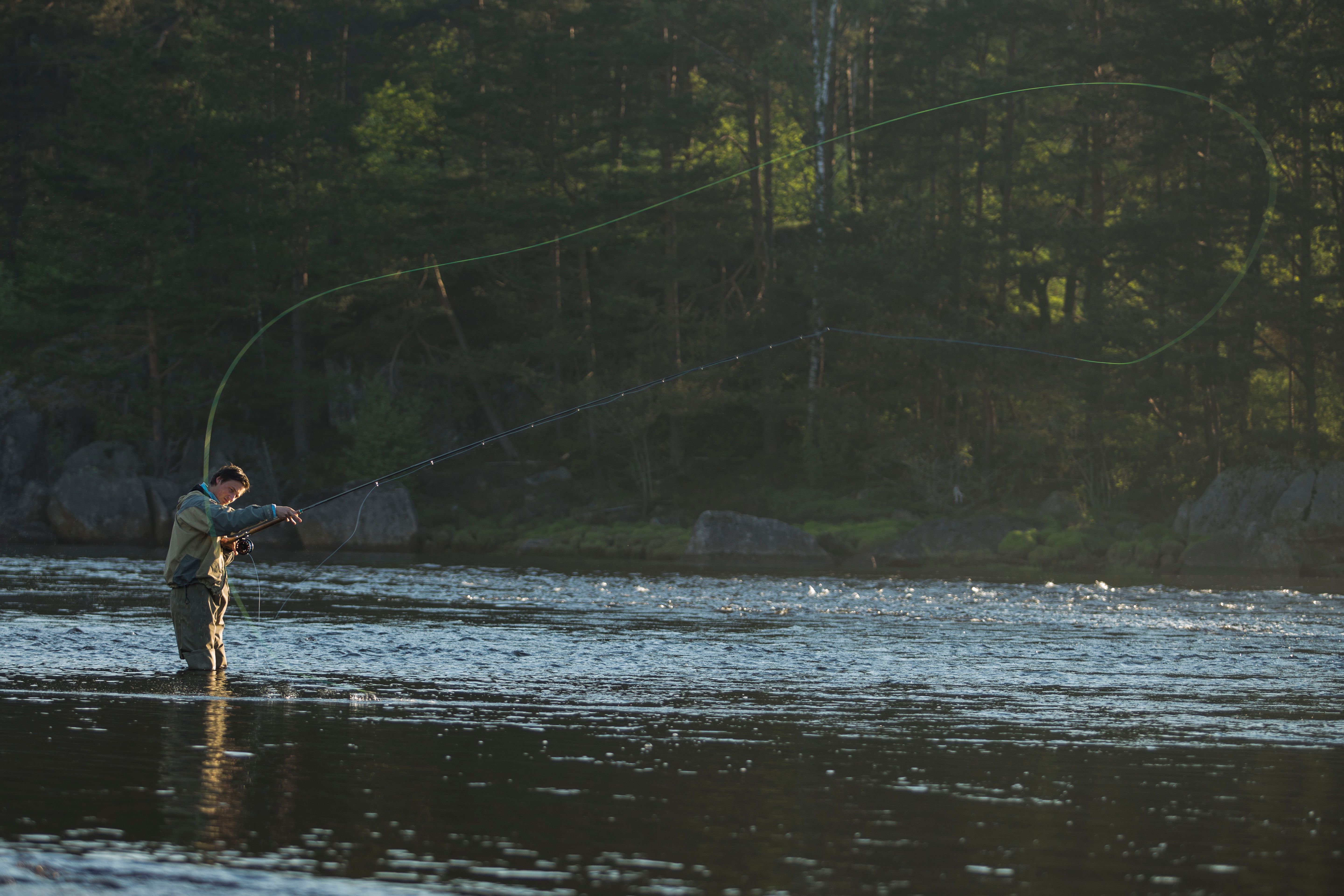 Mann i vadebukse ut i vannet opp til kneet og fluefisker