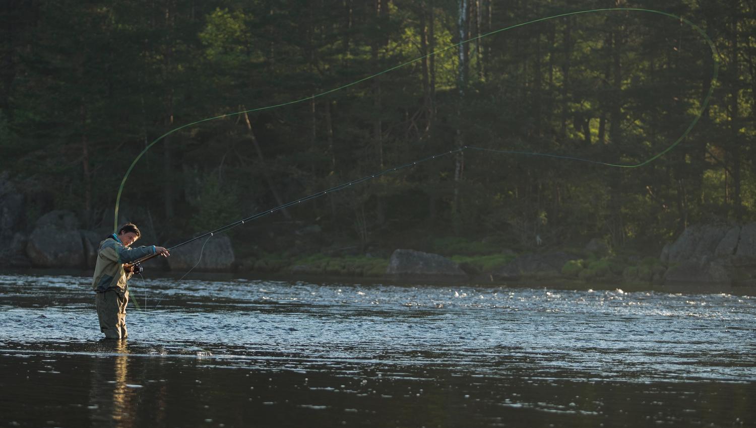 Mann i vadebukse ut i vannet opp til kneet og fluefisker
