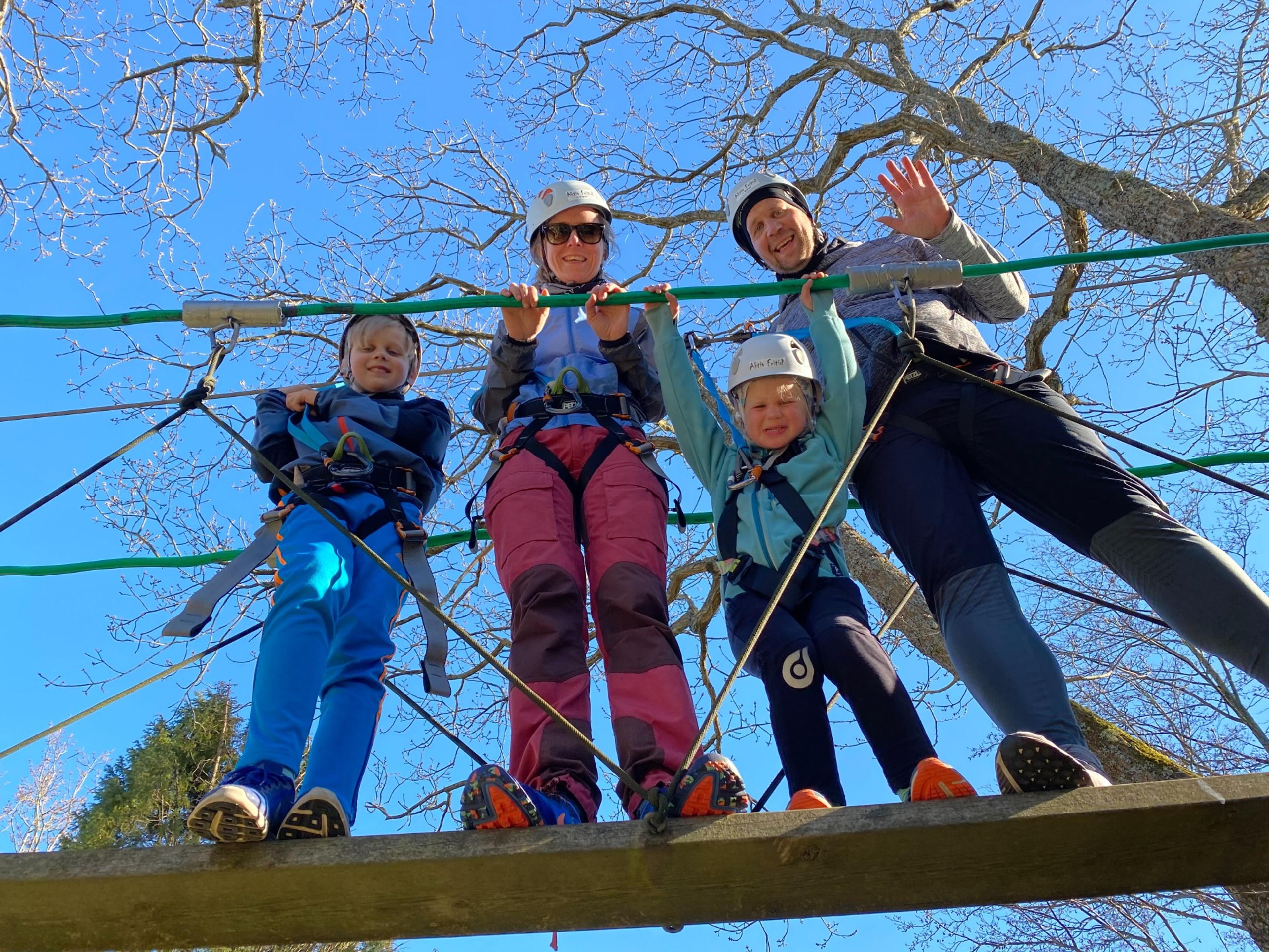 A family of four smiles down from the bridge under the trees
