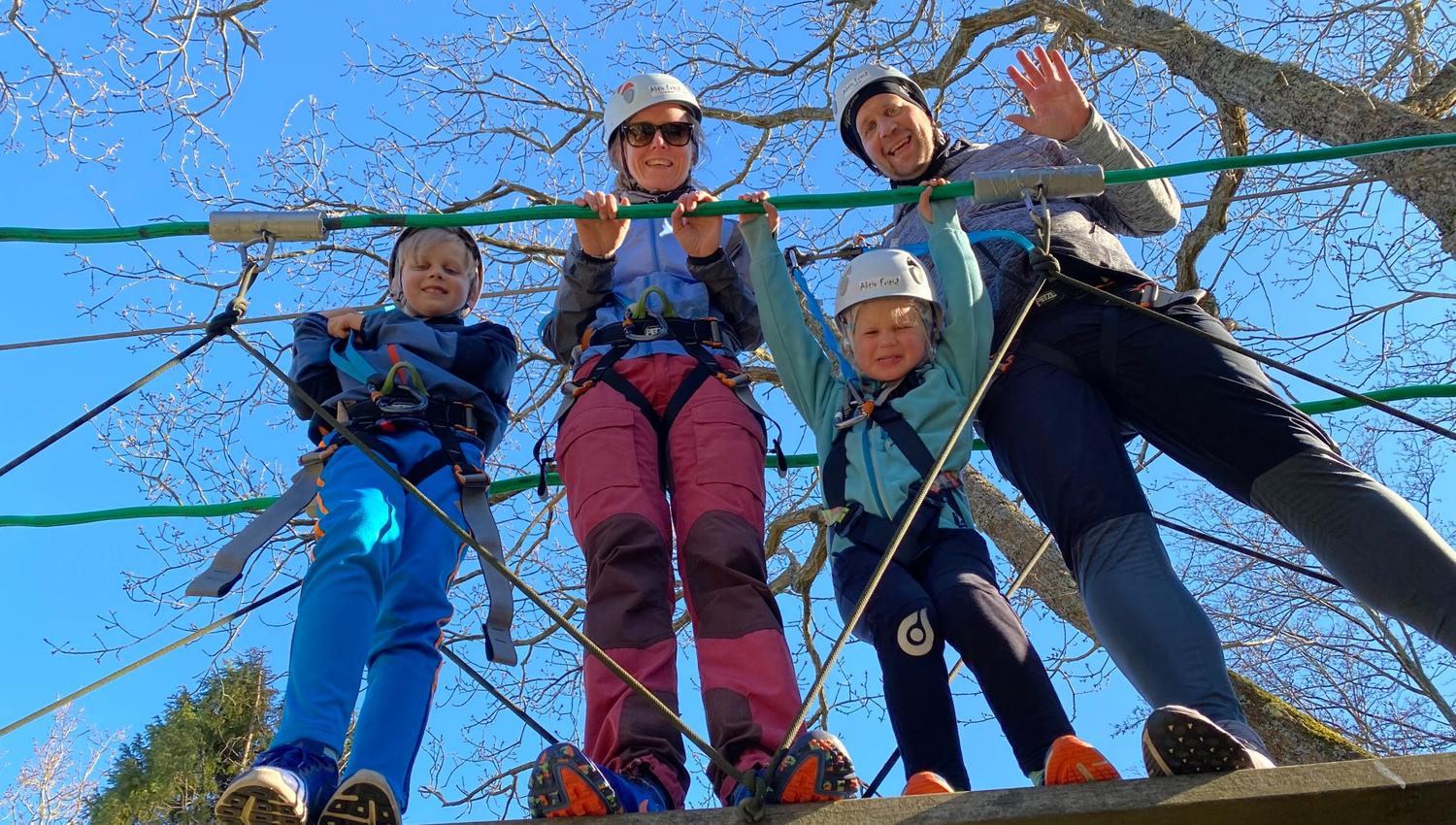 En familie på fire smiler ned fra brua under trærne