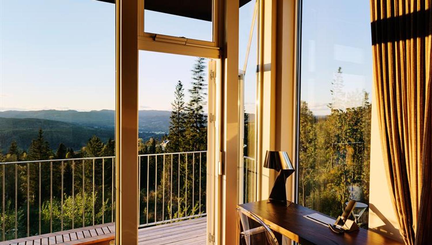 Utsikt over skogen fra rom med skrivepult og balkong. Foto