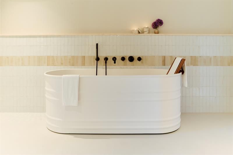 Badet har frittstående badekar, veggmontert armatur og flislagte flater. Utformet for funksjonell og komfortabel bruk.