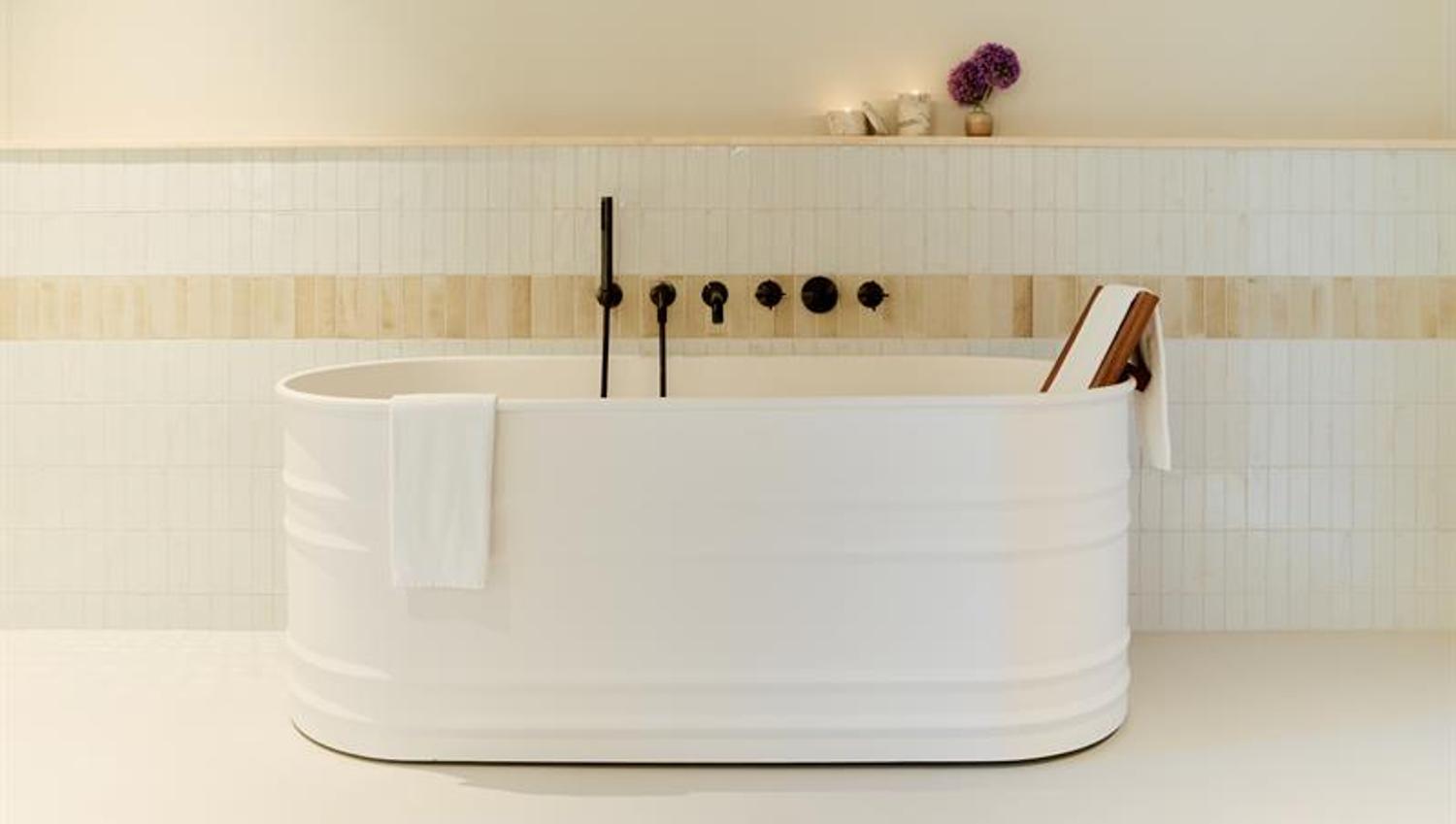 Badet har frittstående badekar, veggmontert armatur og flislagte flater. Utformet for funksjonell og komfortabel bruk.