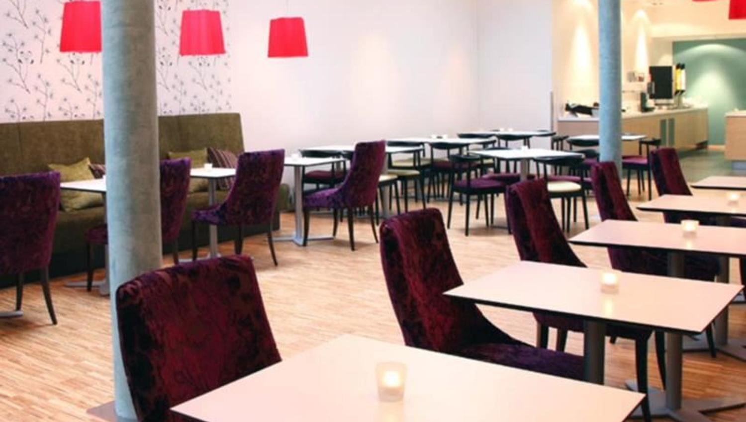 Bright and modern dining area with purple chairs, white tables, and red lamps.