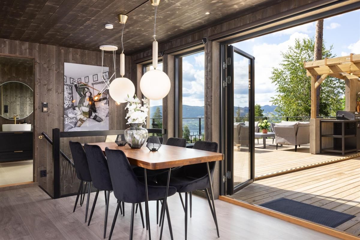 En spisestue med store skyvedører åpne mot en terrasse og utsikt over naturen.