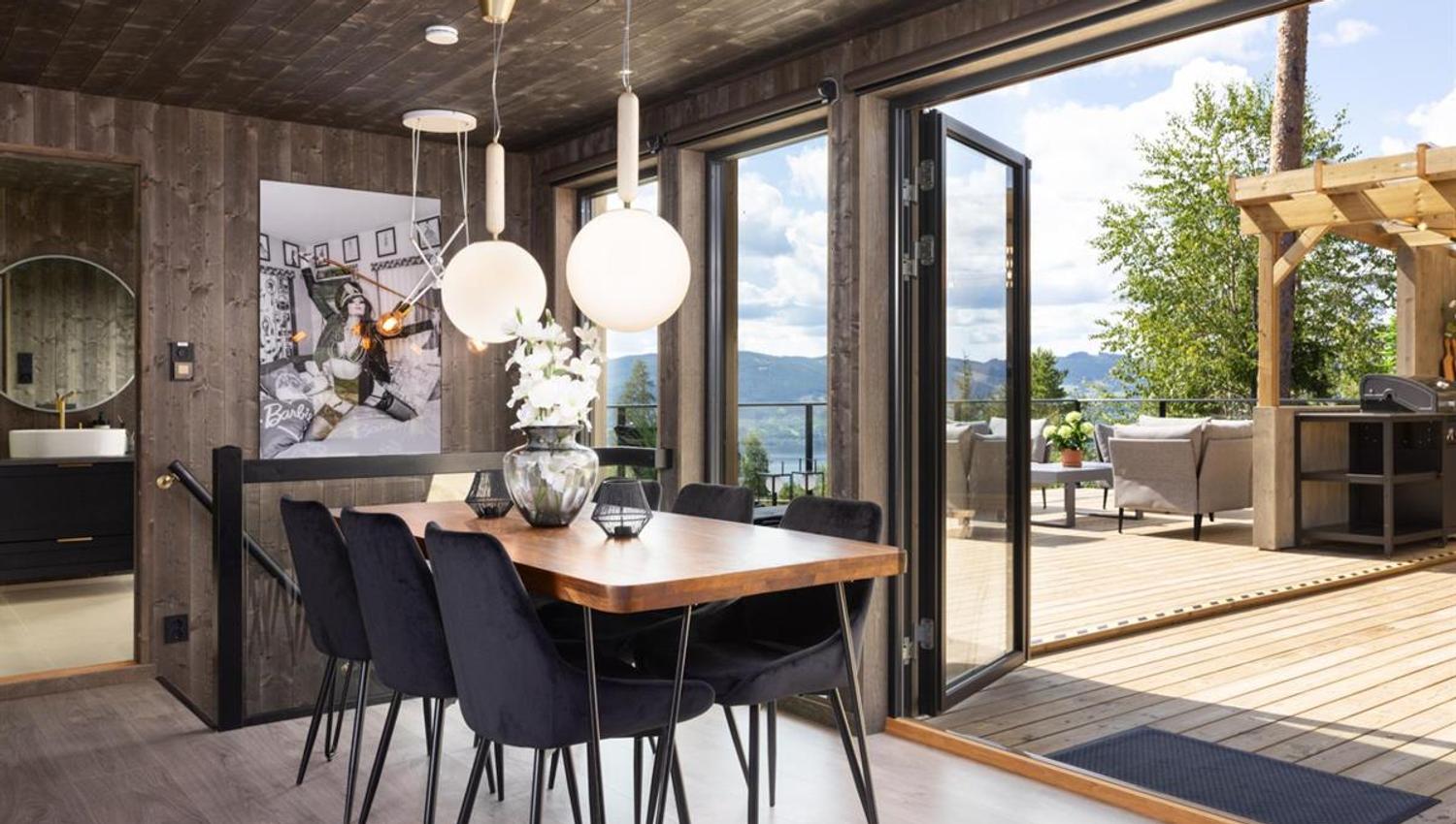 En spisestue med store skyvedører åpne mot en terrasse og utsikt over naturen.
