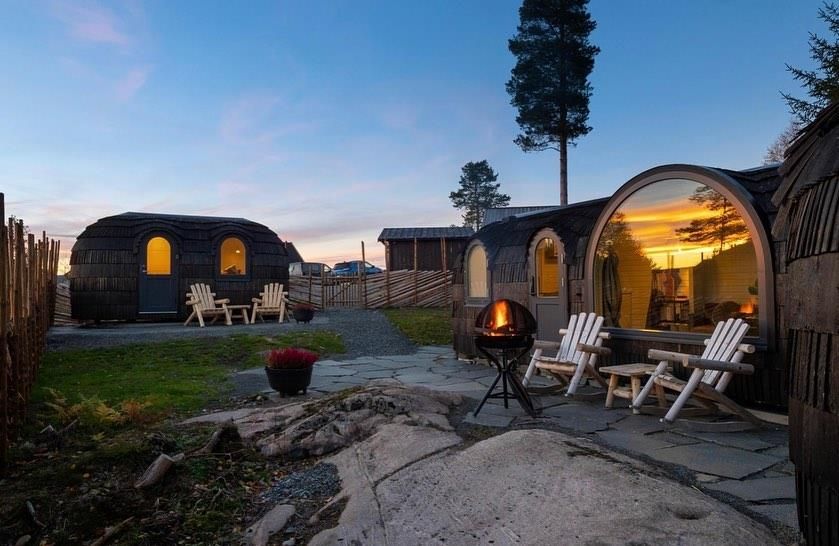 Wooden cabin pods with an outdoor seating area lit at dusk.
