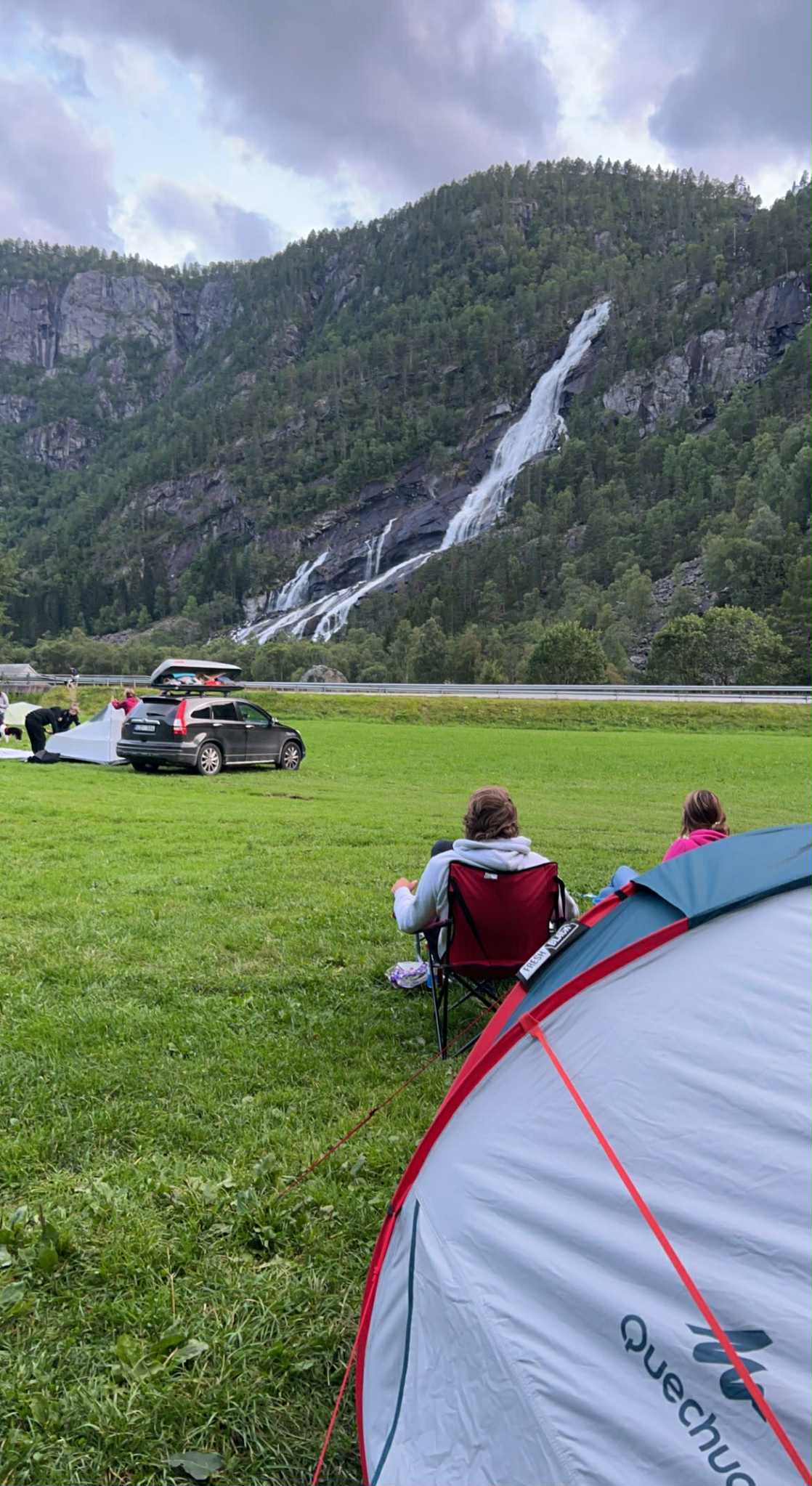 Gjester slappar av ved telt på Hildal Camping med fossen som bakteppe.