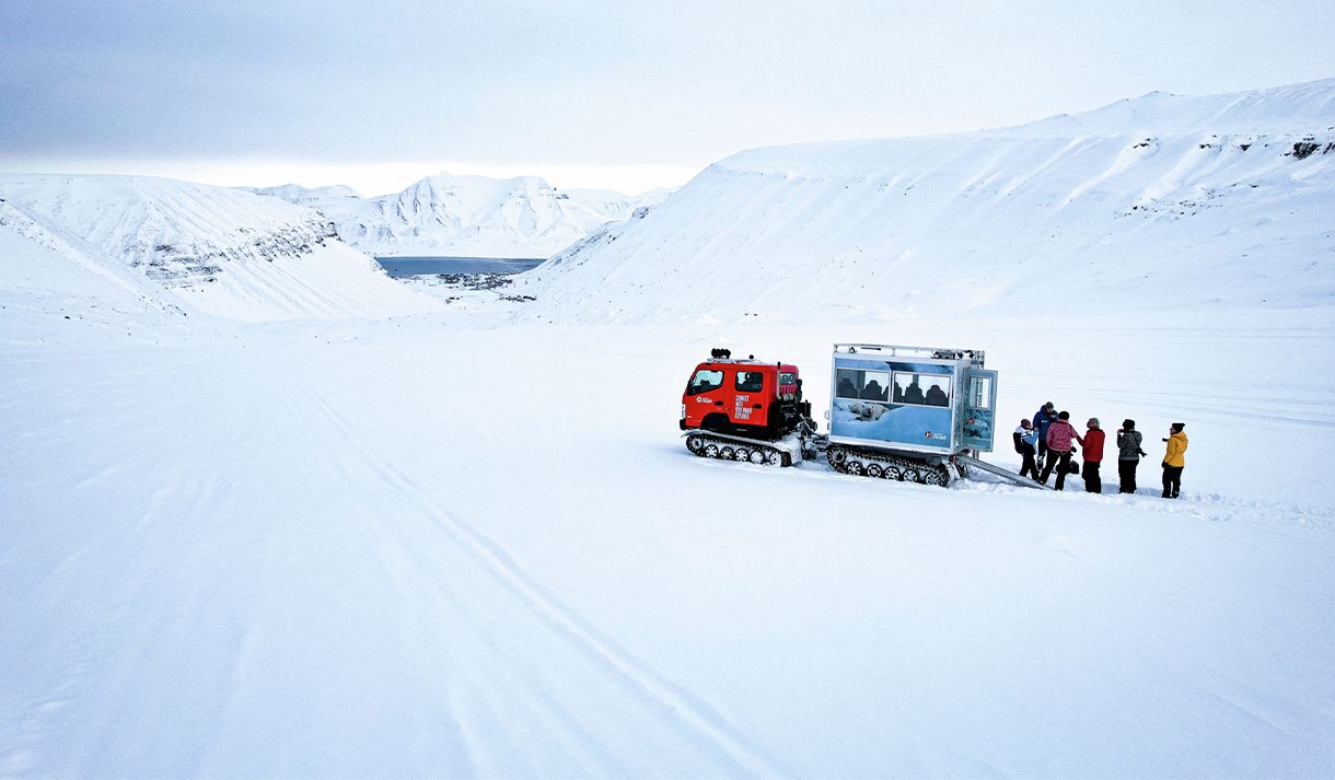 Guests and a guide standing next to a snowcat on top of a glacier surrounded by snow-covered mountains