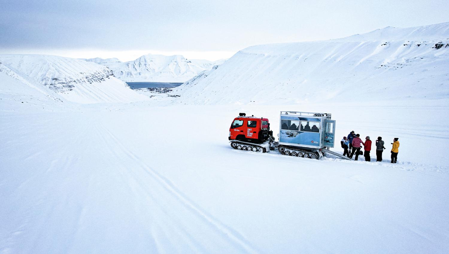 Guests and a guide standing next to a snowcat on top of a glacier surrounded by snow-covered mountains