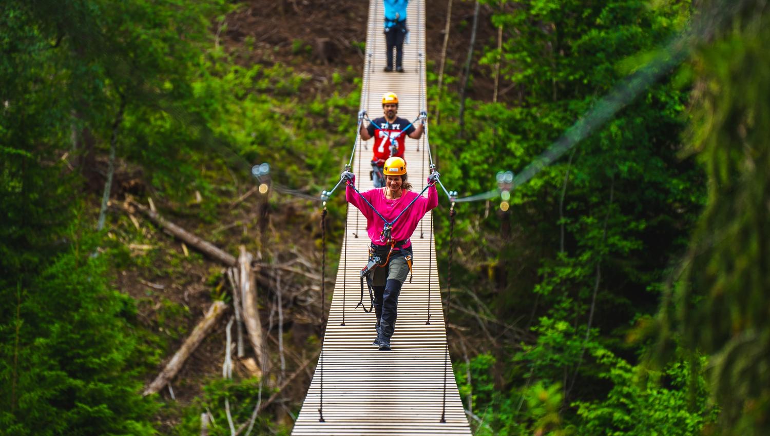 Tre personer som går over hengebroa i Via ferrata Haldenkanalen