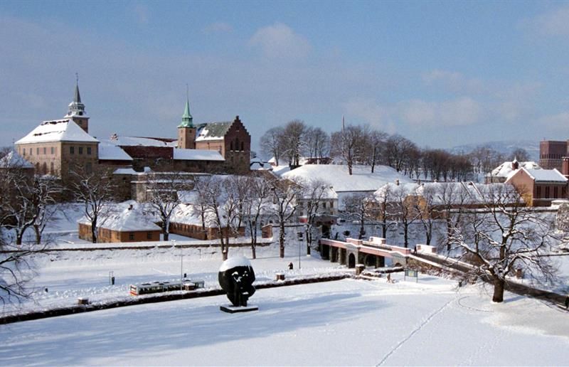 Vinterbilde av festningen dekket i snø, sett fra avstand. Rådhuset i bakgrunnen på høyre side.