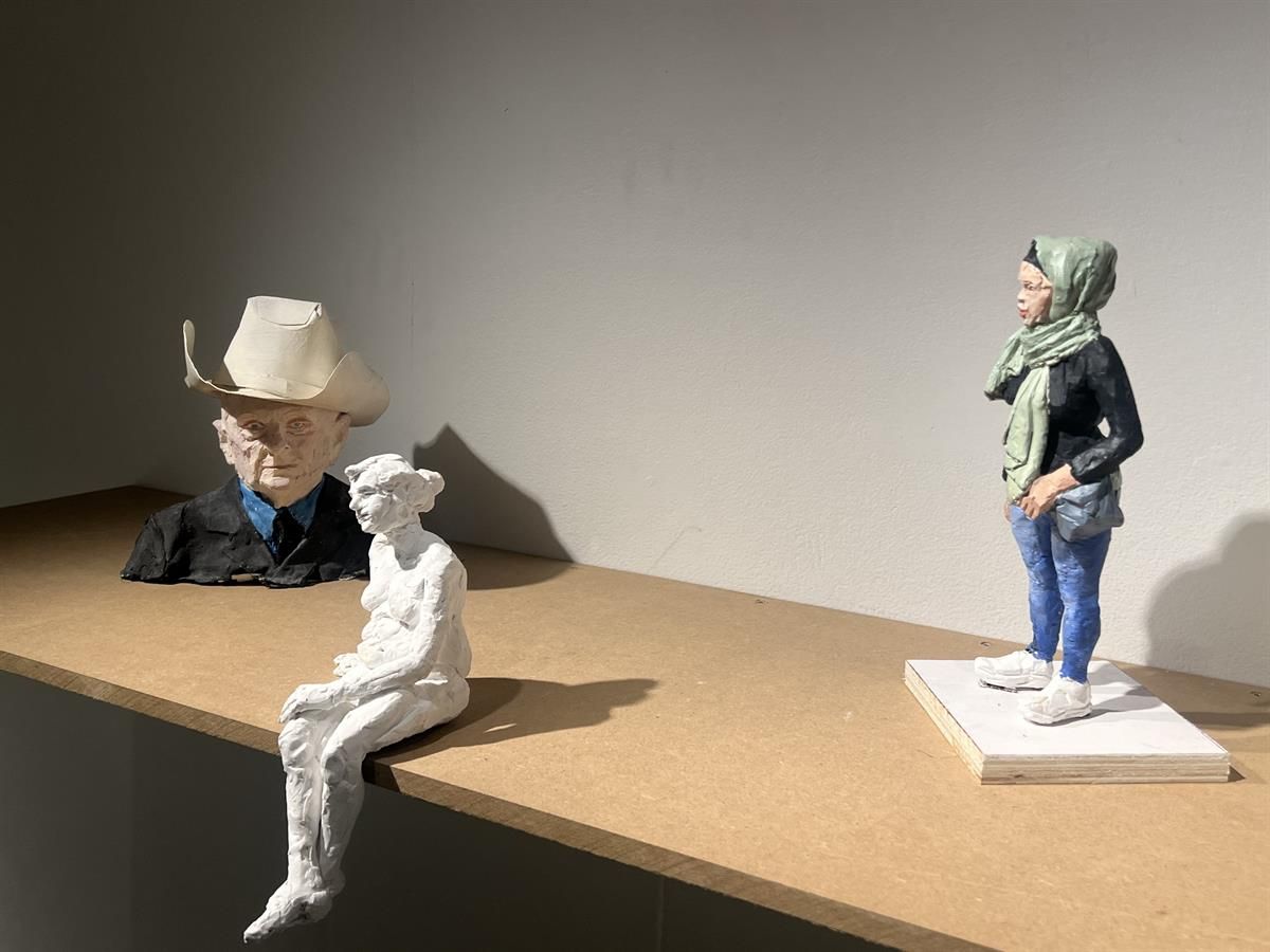 Skulpturer av figurer plassert på en treflate i galleri.