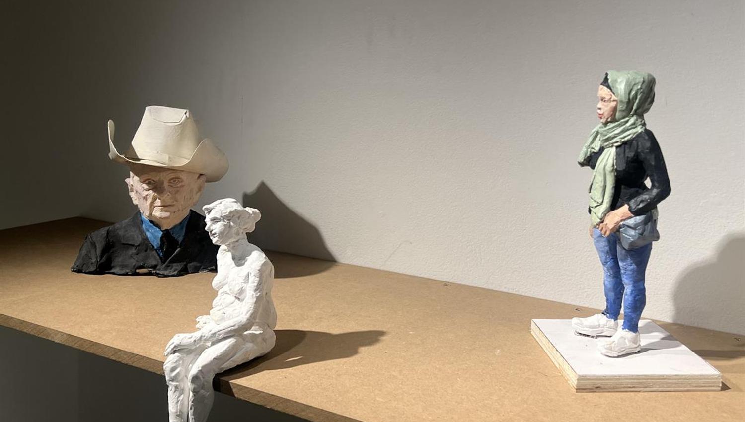 Skulpturer av figurer plassert på en treflate i galleri.
