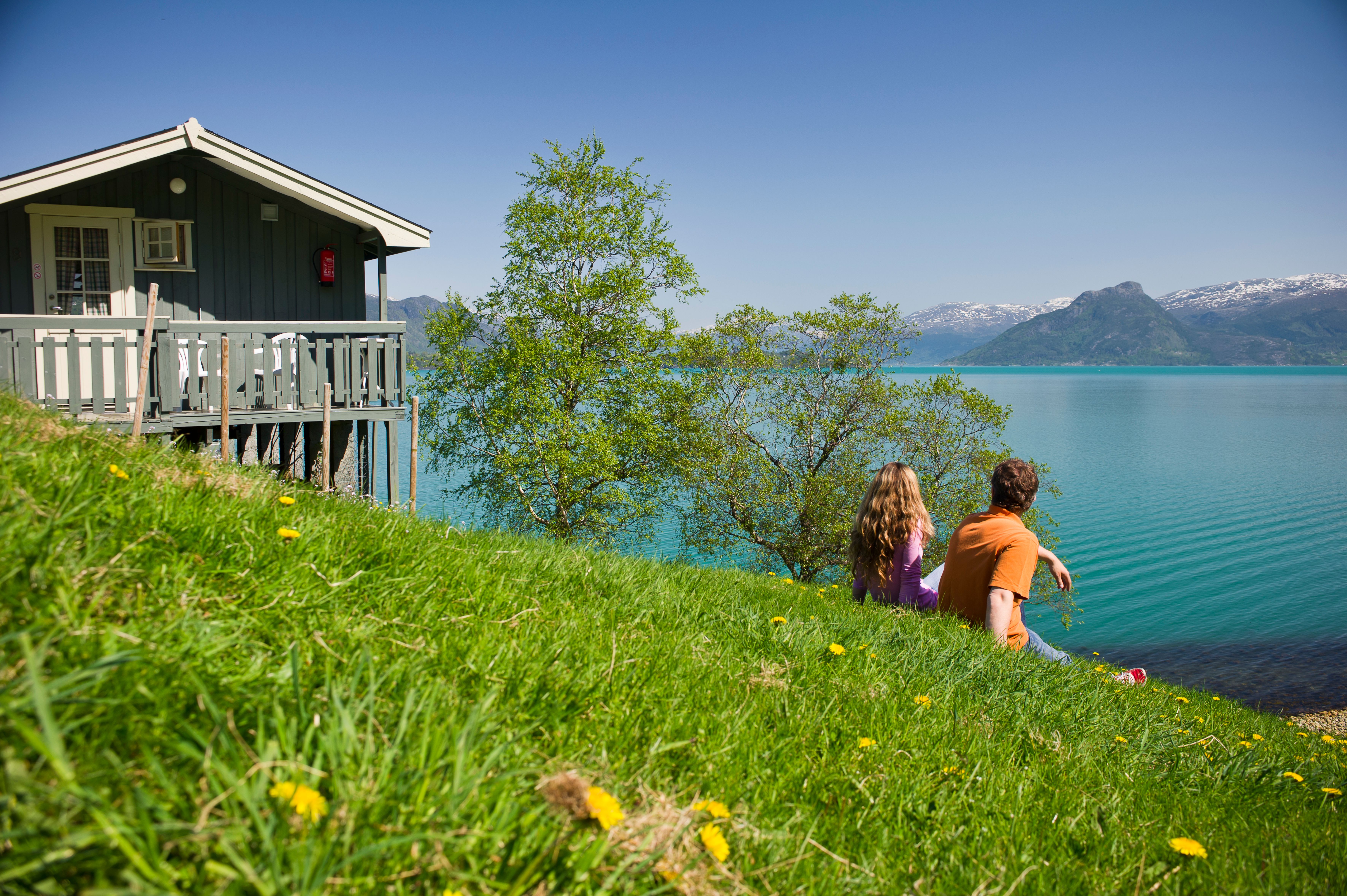 Par nyt utsikta frå Oddland Camping mot fjorden og snødekte fjell.