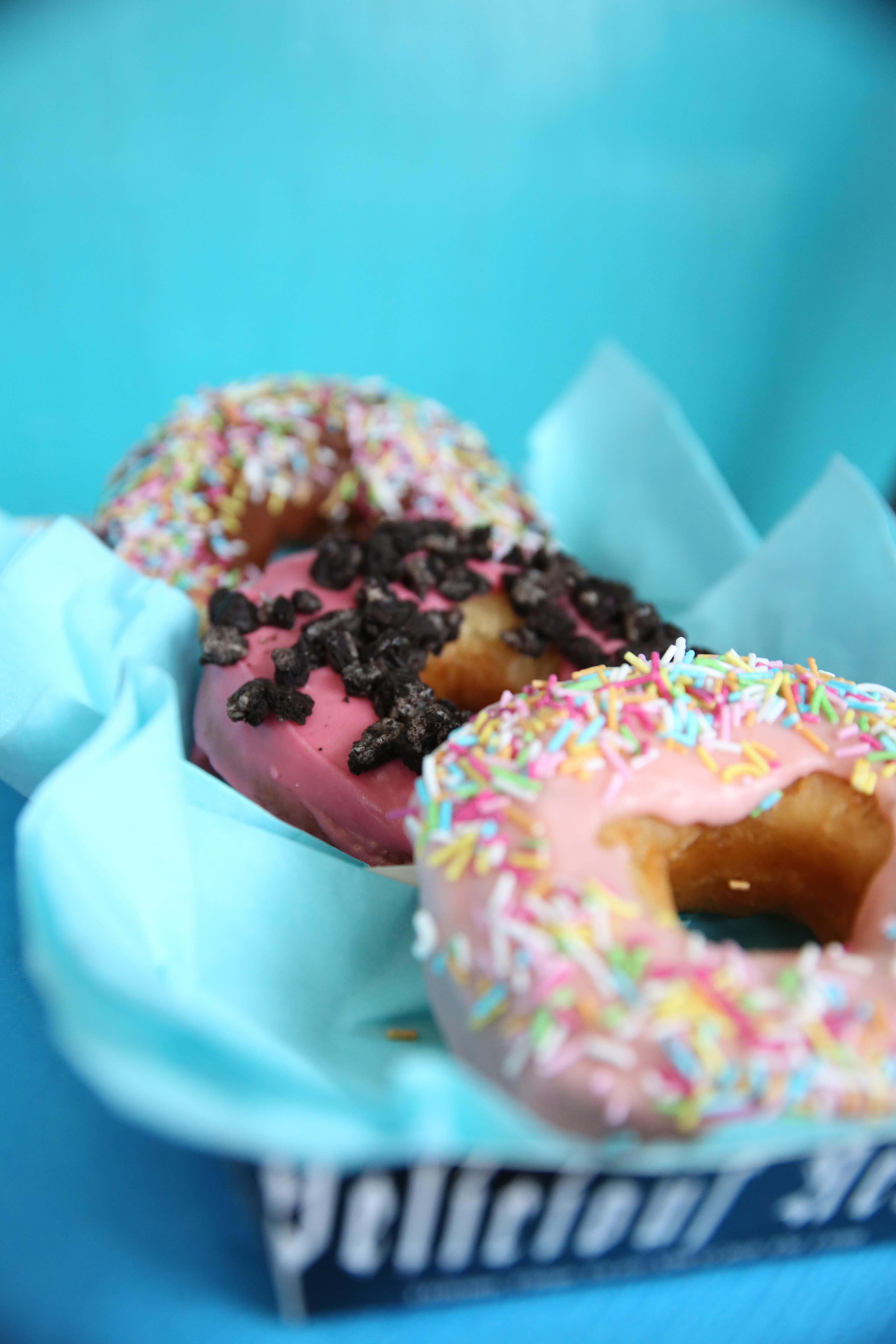 Tre donuts med forskjellig topping mot turkis bakgrunn. Foto.
