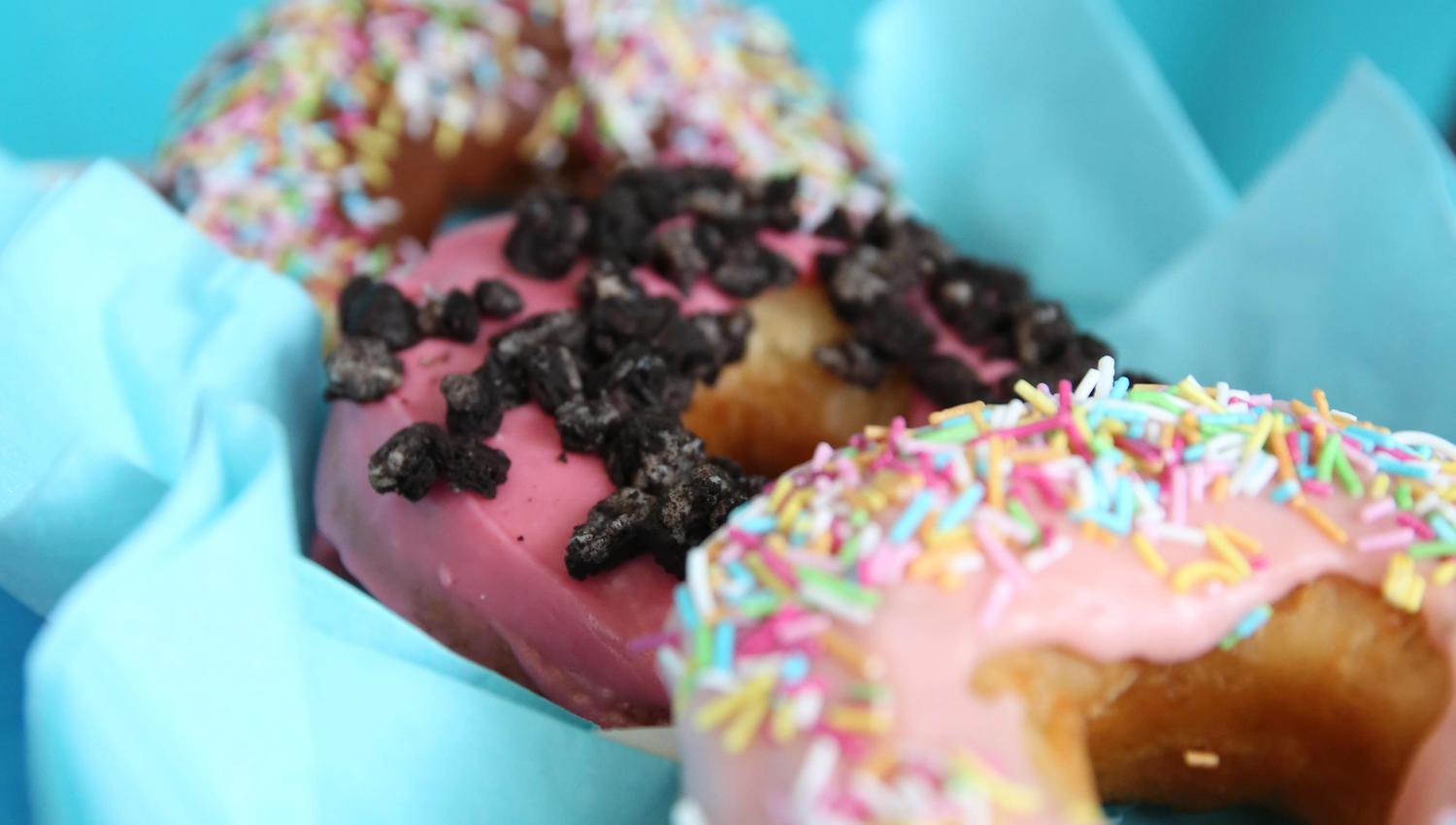 Tre donuts med forskjellig topping mot turkis bakgrunn. Foto.