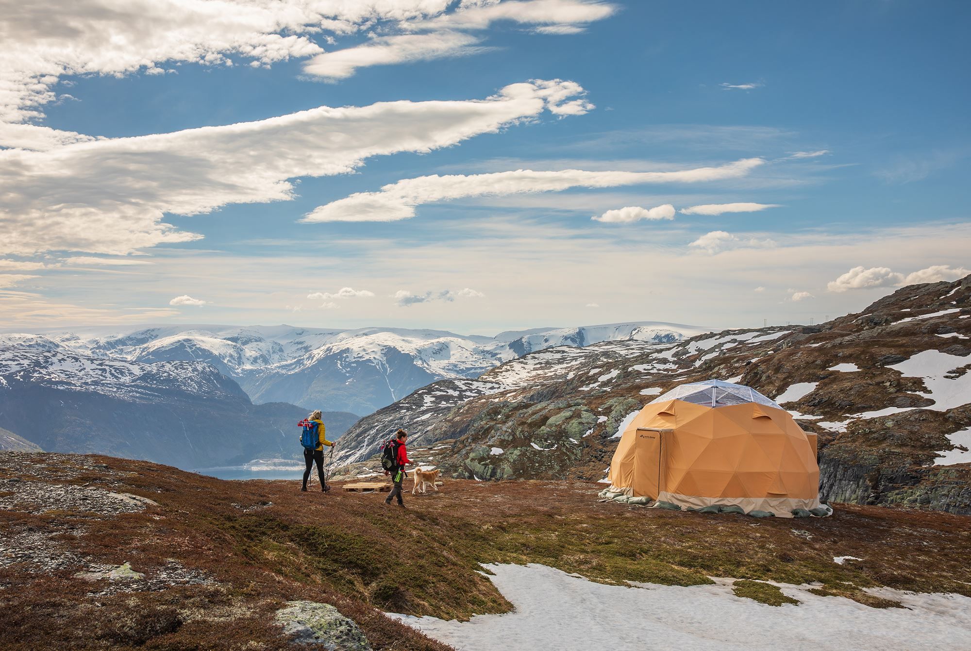 Hikers and a dog by a glamping dome with panoramic fjord and mountain views near Trolltunga.