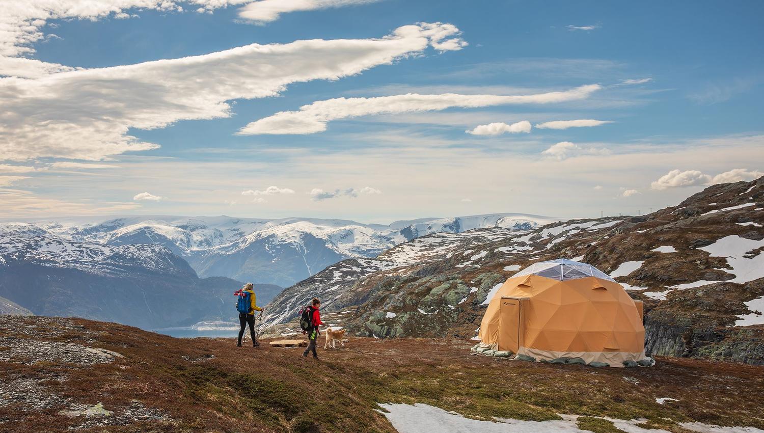 Hikers and a dog by a glamping dome with panoramic fjord and mountain views near Trolltunga.