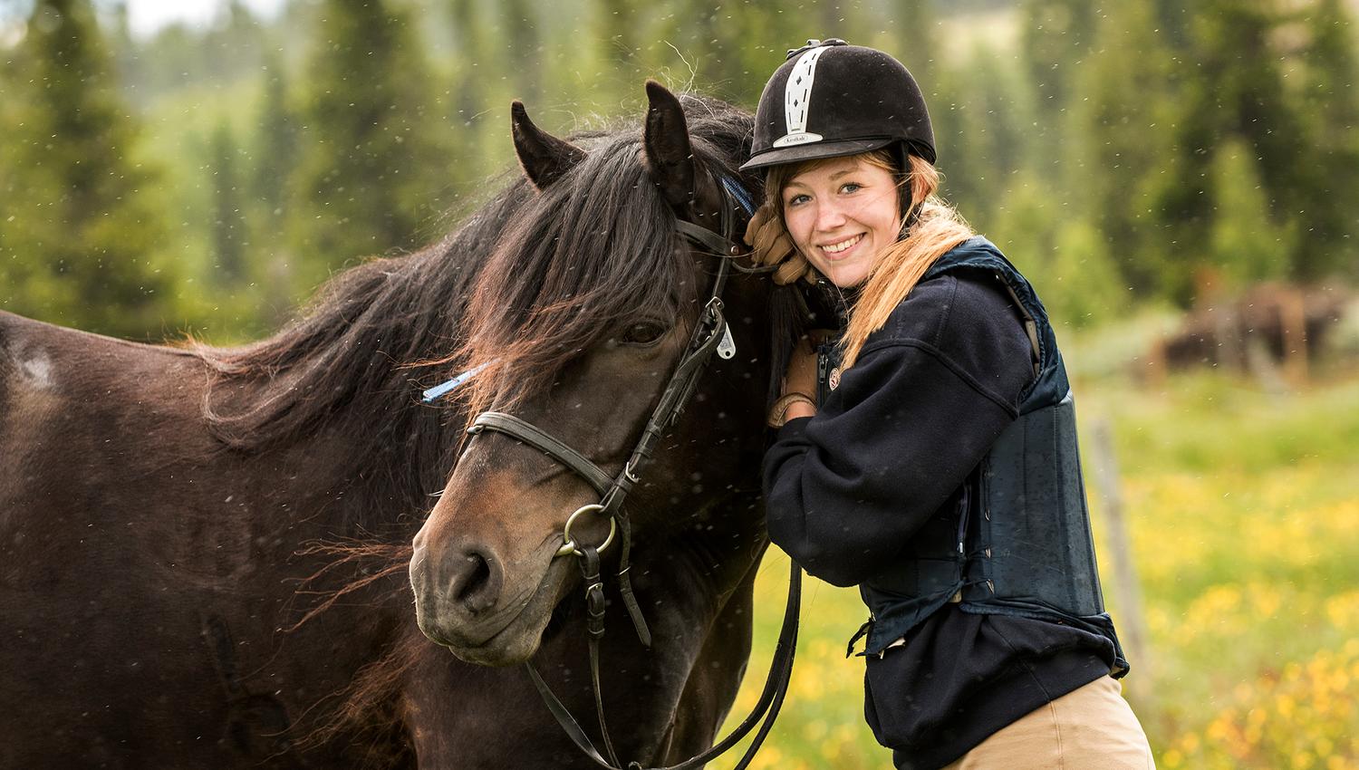 A young woman smiles towards the camera with her horse