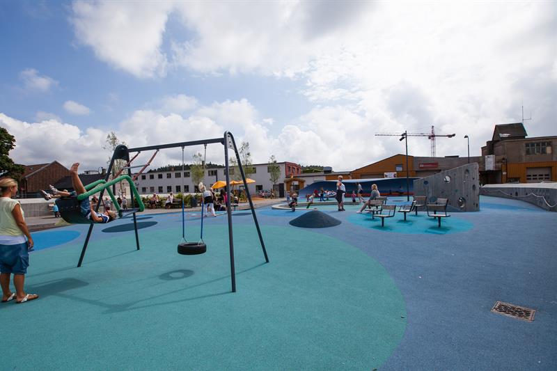 Buen Playground, blue in different shades on the ground with many different play equipment. Trampoline, swing, climbing wall, balance line.