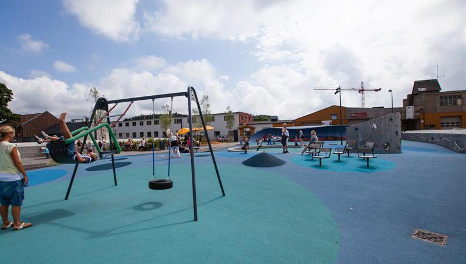 Buen Playground, blue in different shades on the ground with many different play equipment. Trampoline, swing, climbing wall, balance line.