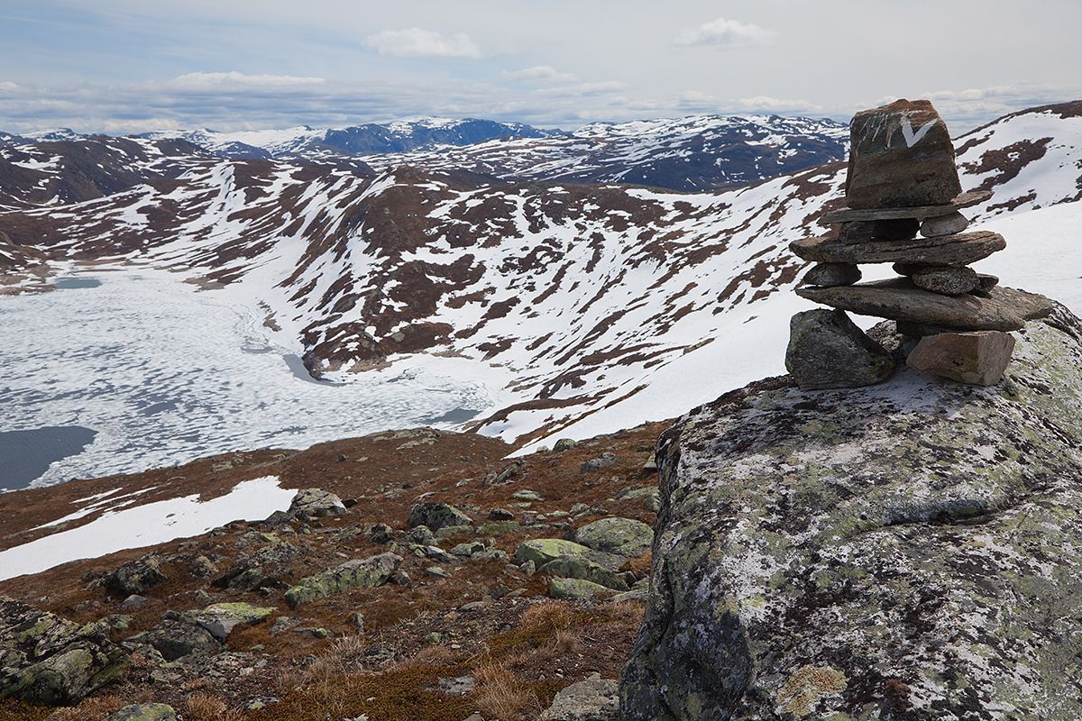 A cairn of stones with a white V markes the path to Horntind. It's early in the season, and the mountain landscape beyond is still largely snow-covere