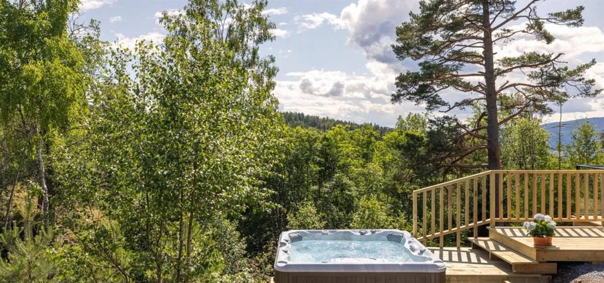 En badestamp på en terrasse omgitt av trær og utsikt over naturen.