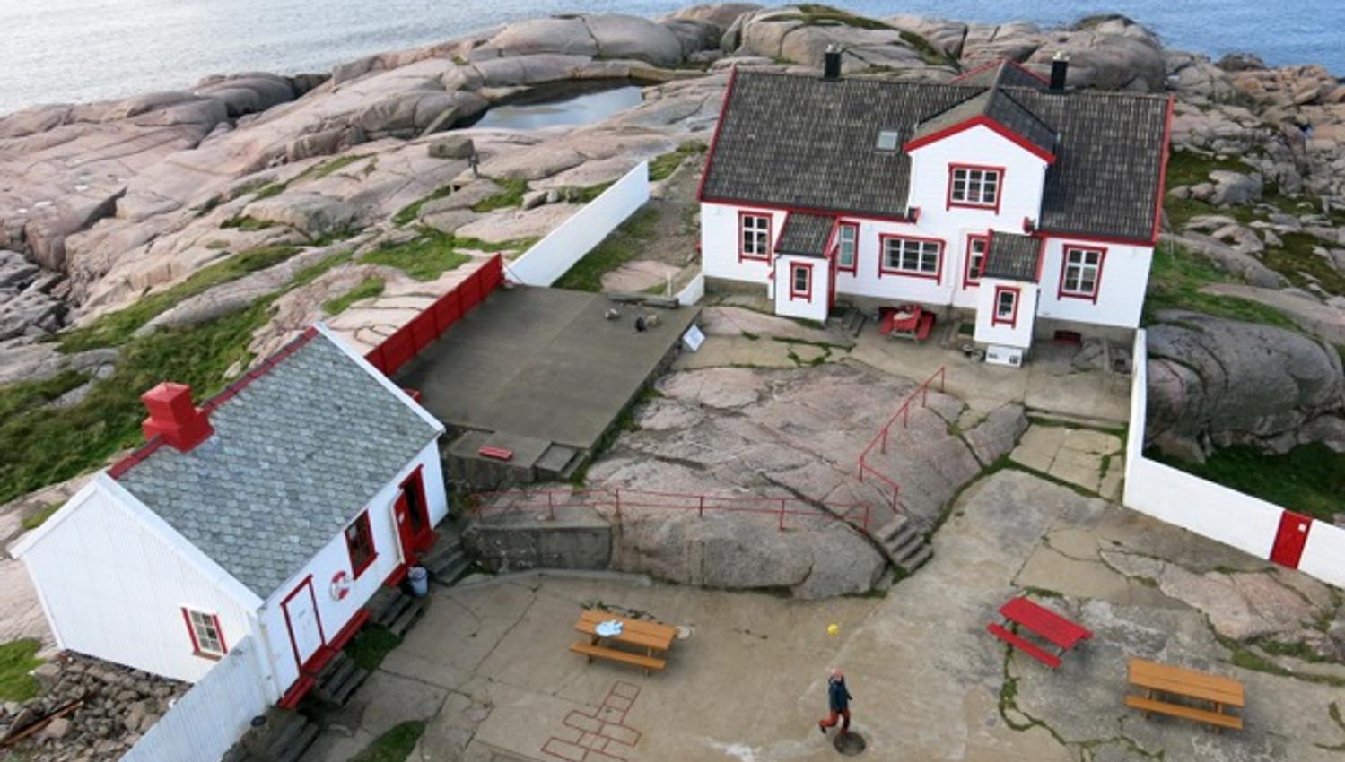 Overview image of the house at Ryvingen Lighthouse. The house is white with red details (red trim) and a black roof.