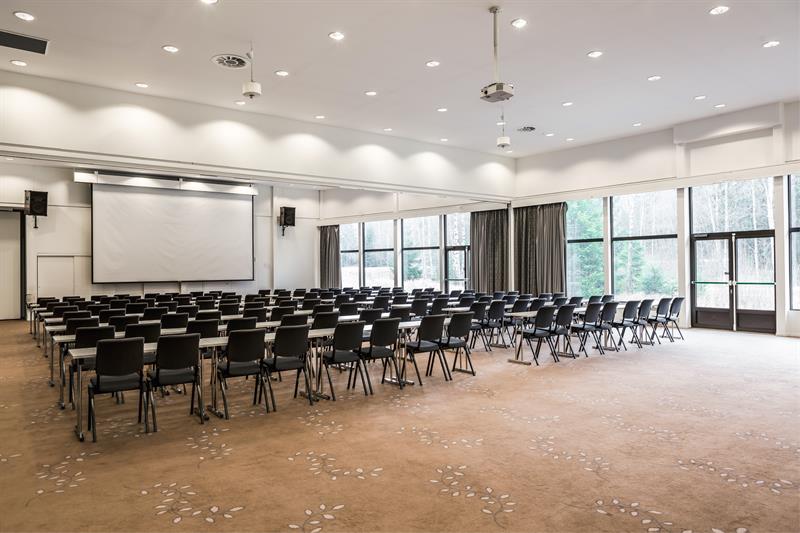 Stort konferanserom med mange stoler og scene, tilrettelagt for arrangementer.