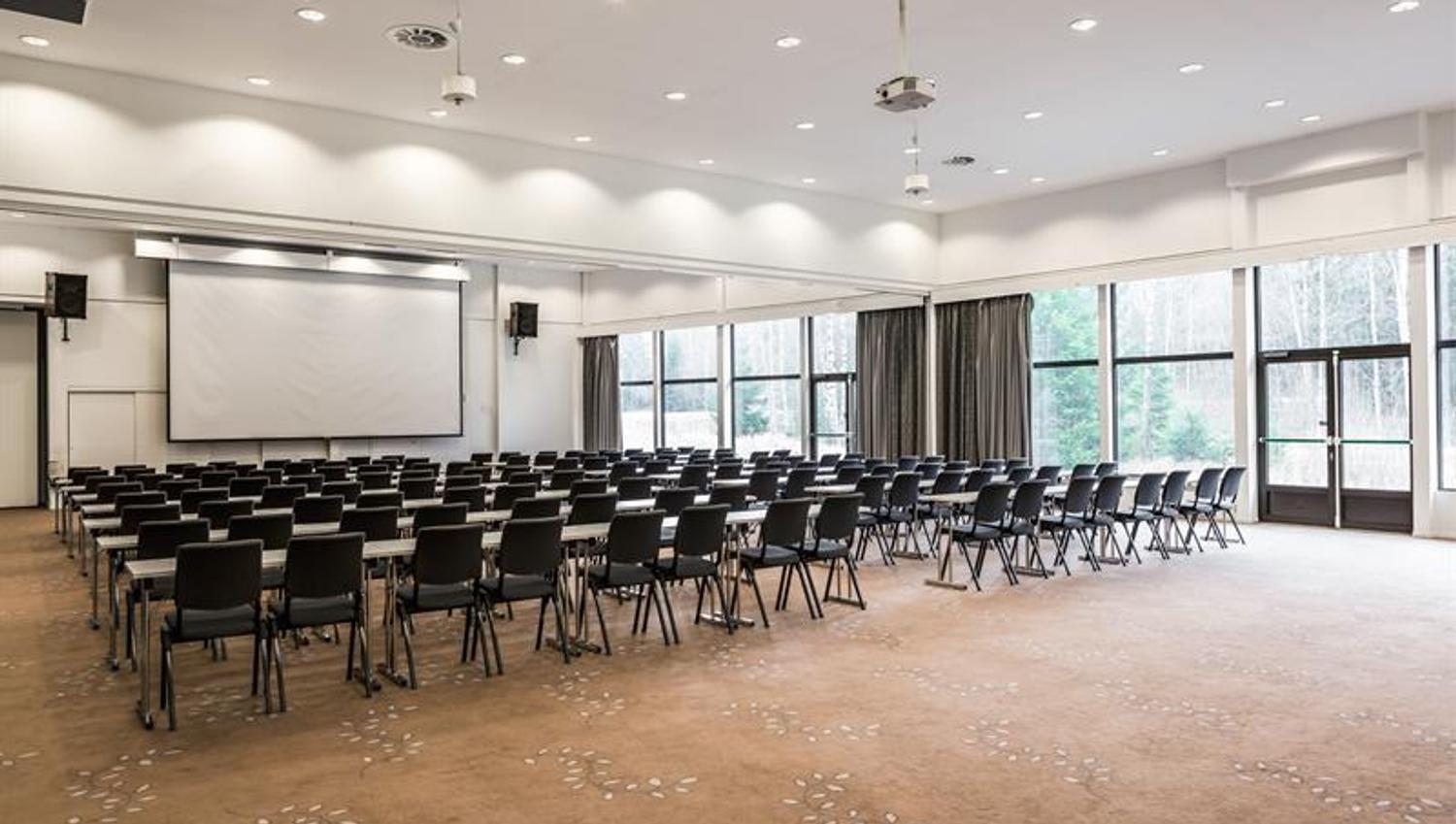 Stort konferanserom med mange stoler og scene, tilrettelagt for arrangementer.