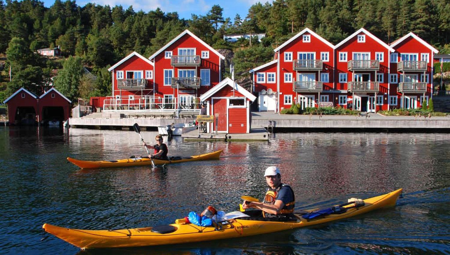 Bilde fra vannet mot de røde bygningene på Tregde, med to personer i hver sin gul kajakk
