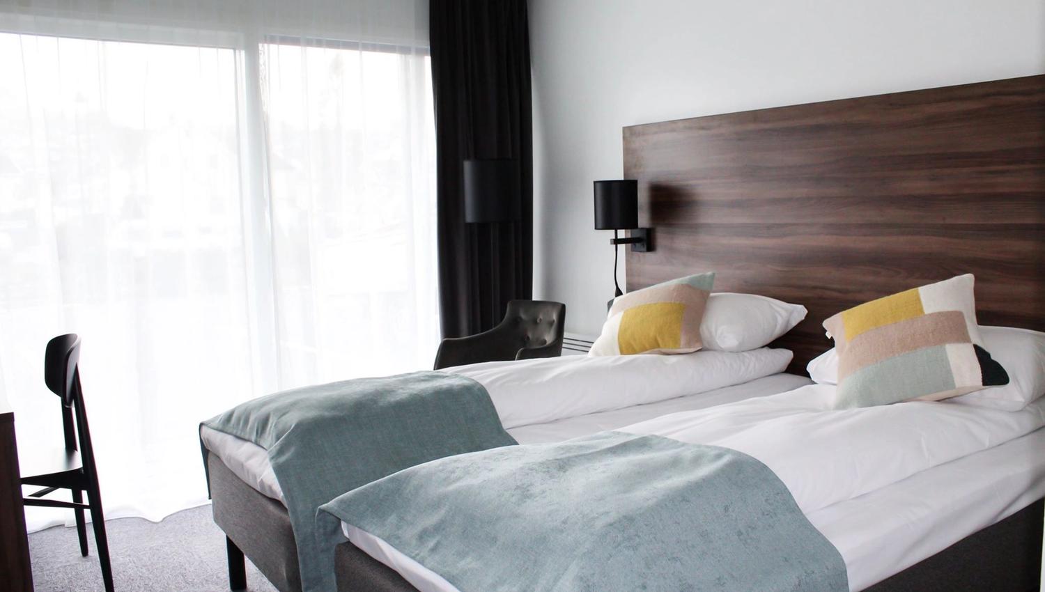 Lyst hotellrom med to enkeltsenger og utsikt mot fjorden frå balkongen.