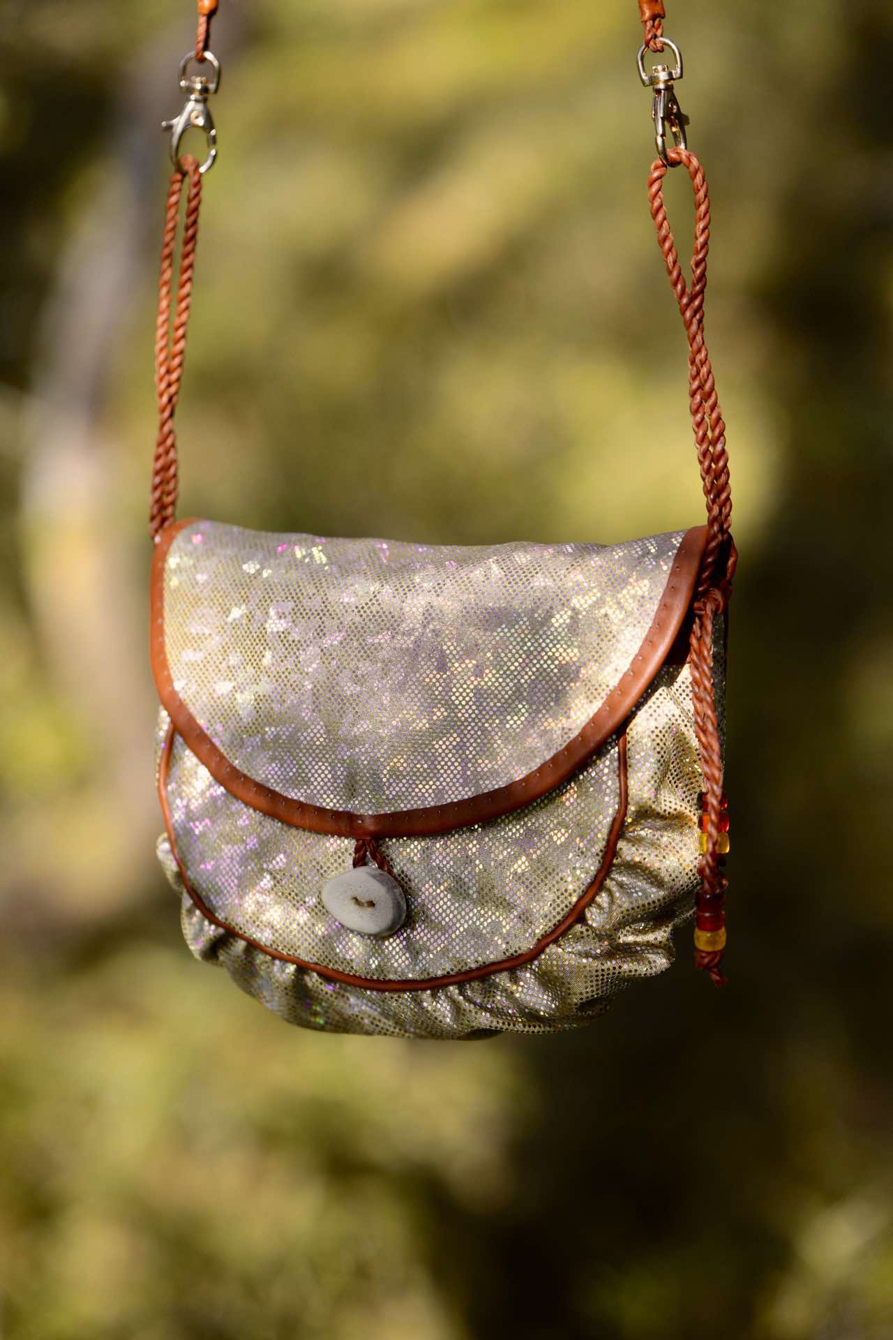 A holographic Sami inspired handbag hanging from a branch in the woods