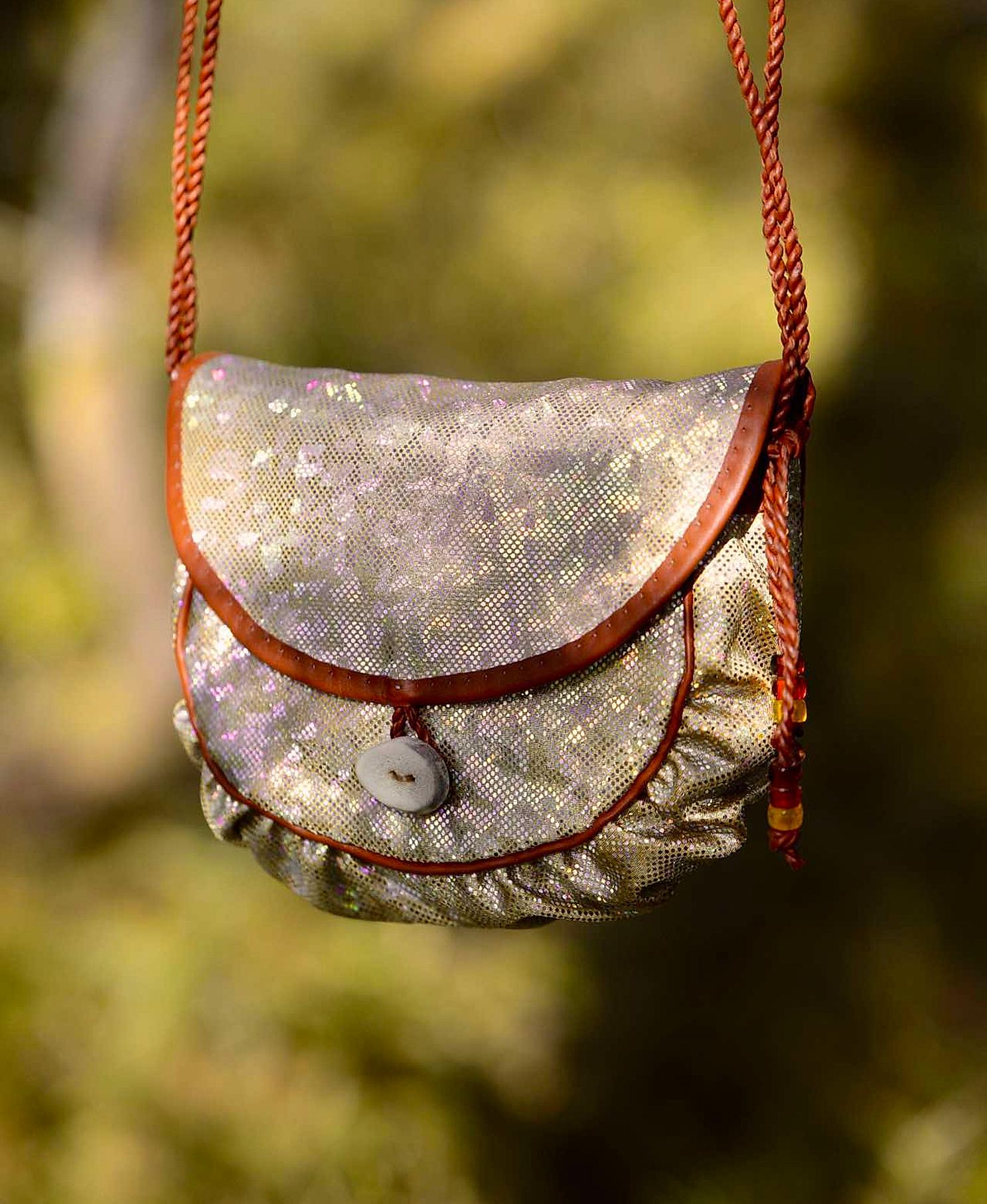 A holographic Sami inspired handbag hanging from a branch in the woods
