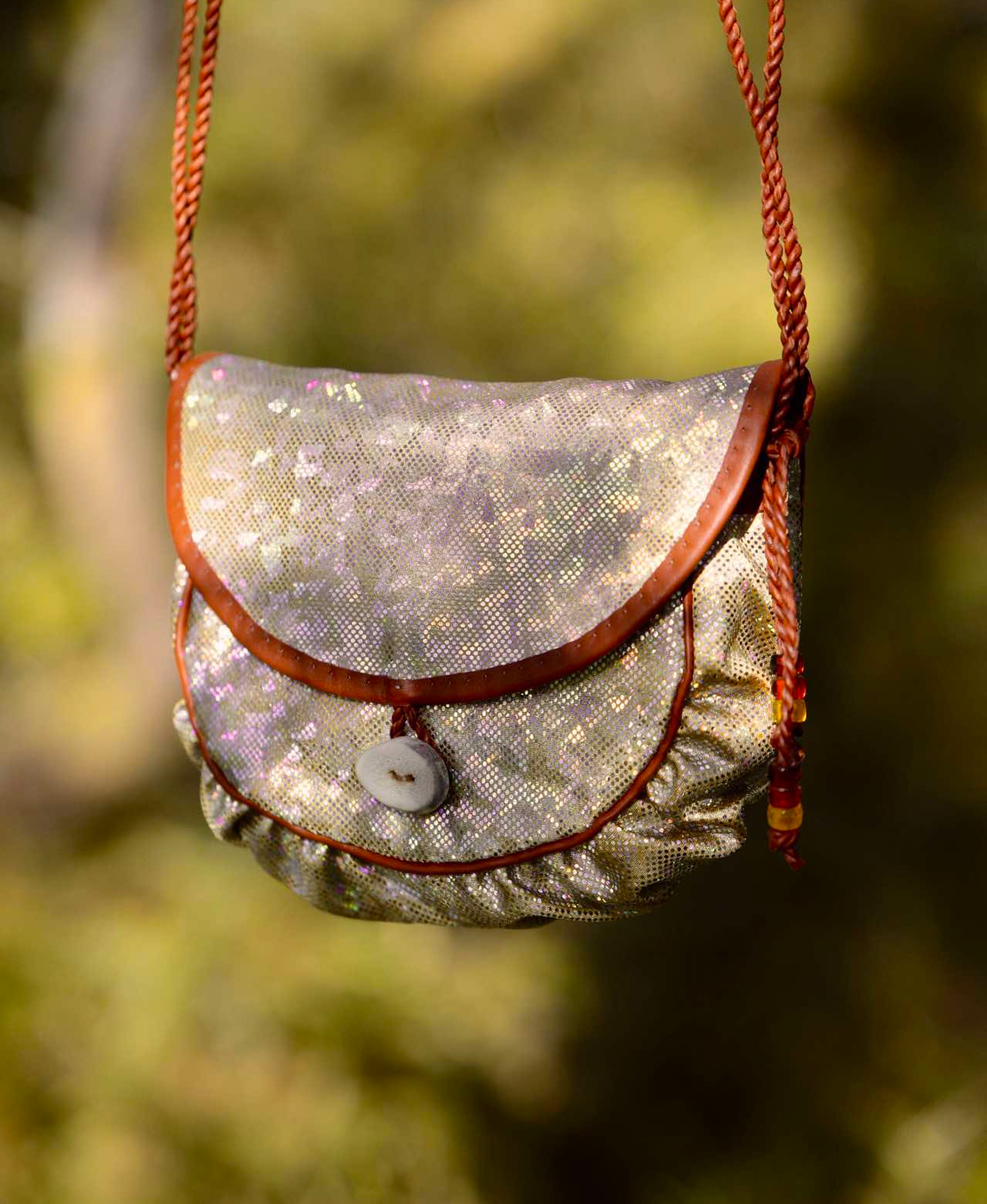 A holographic Sami inspired handbag hanging from a branch in the woods
