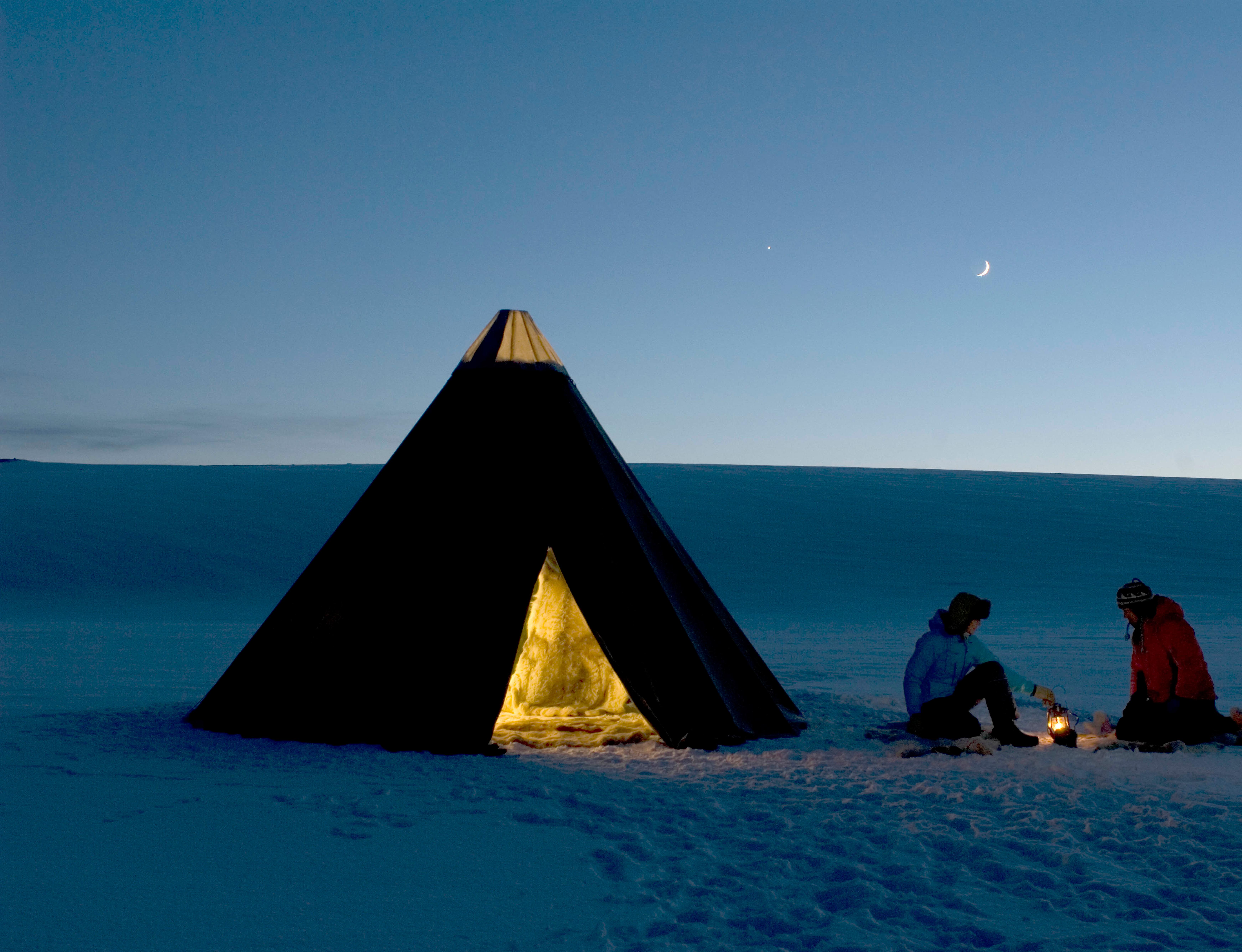 Two people around a fire next to a traditional Sami tent, known as a Lavvo