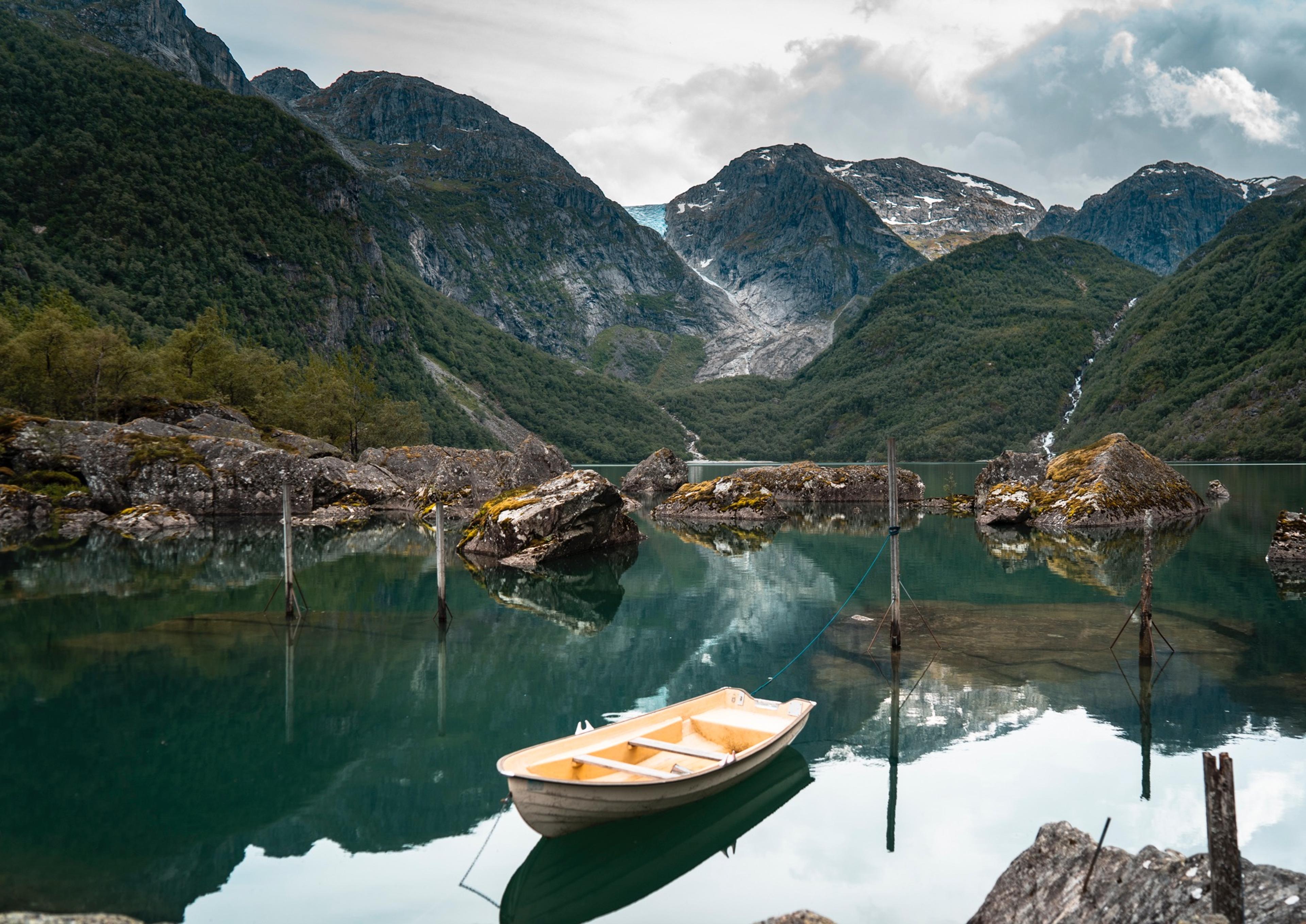 A rowing boat on quiet, turquoise water in the Hardangerfjord region, with mountains and a glacier in the background. Fjord Norway.