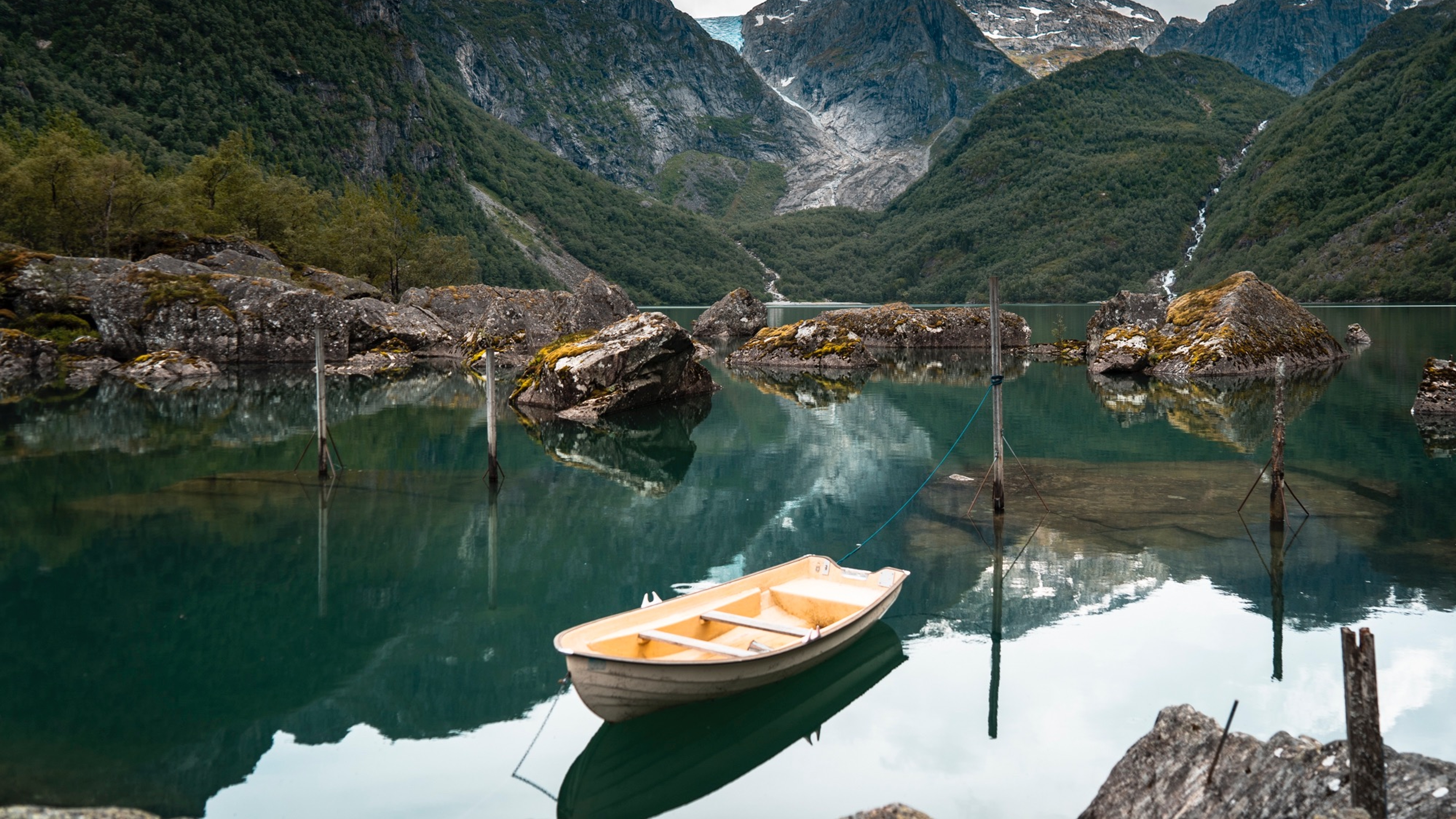 A rowing boat on quiet, turquoise water in the Hardangerfjord region, with mountains and a glacier in the background. Fjord Norway.