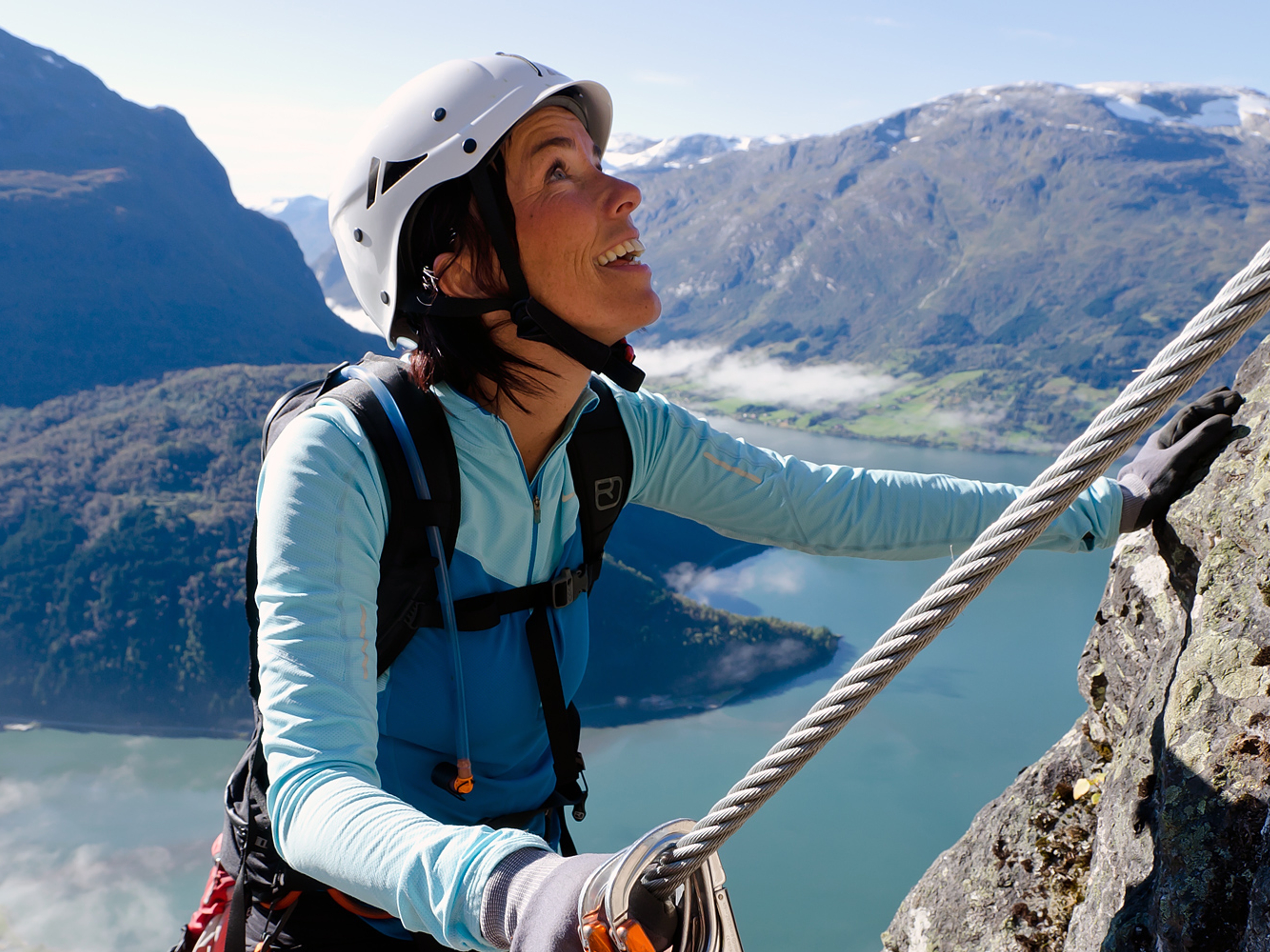 A woman climbing a mountainside on a sunny day in Loen in Fjord Norway
