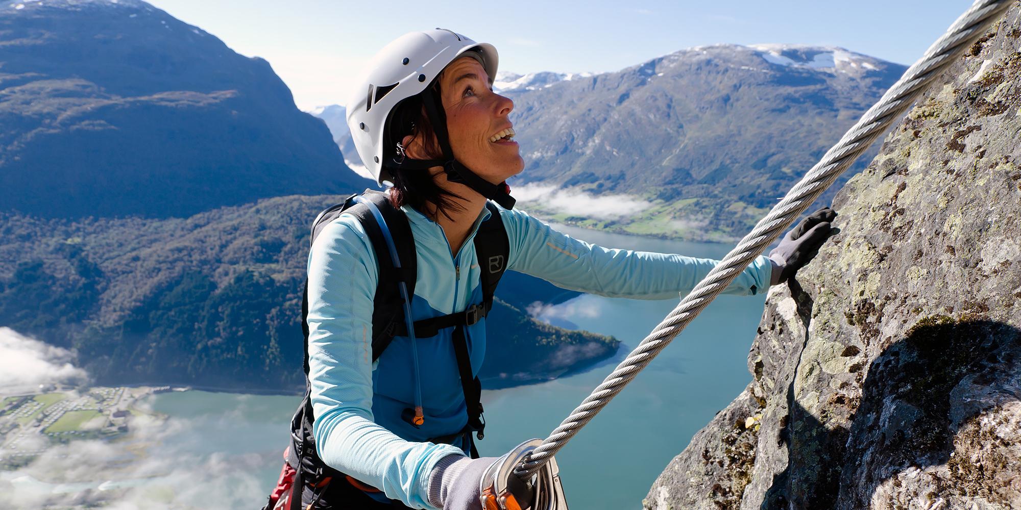 A woman climbing a mountainside on a sunny day in Loen in Fjord Norway