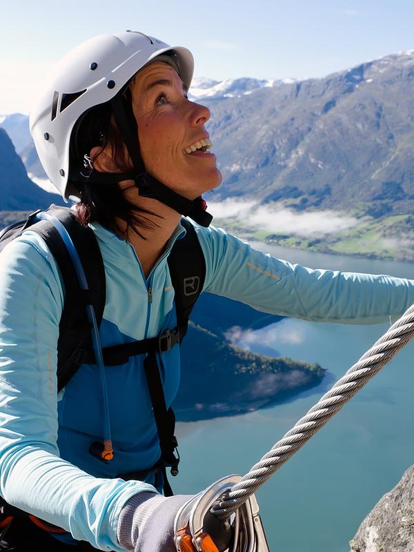 A woman climbing a mountainside on a sunny day in Loen in Fjord Norway