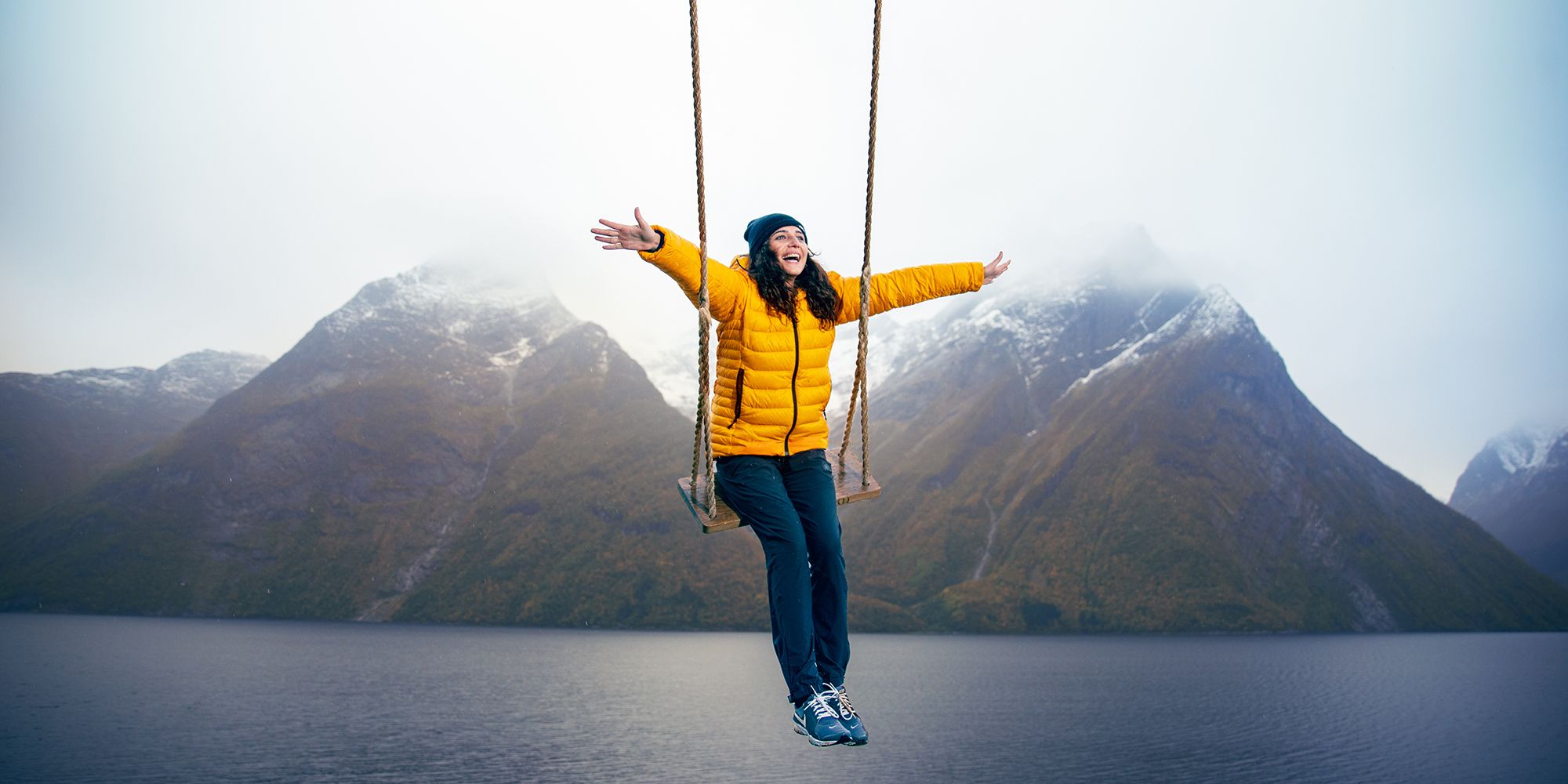 En person gungar vid Hjørundfjorden i regionen Fjord Norge med snöklädda fjäll i bakgrunden