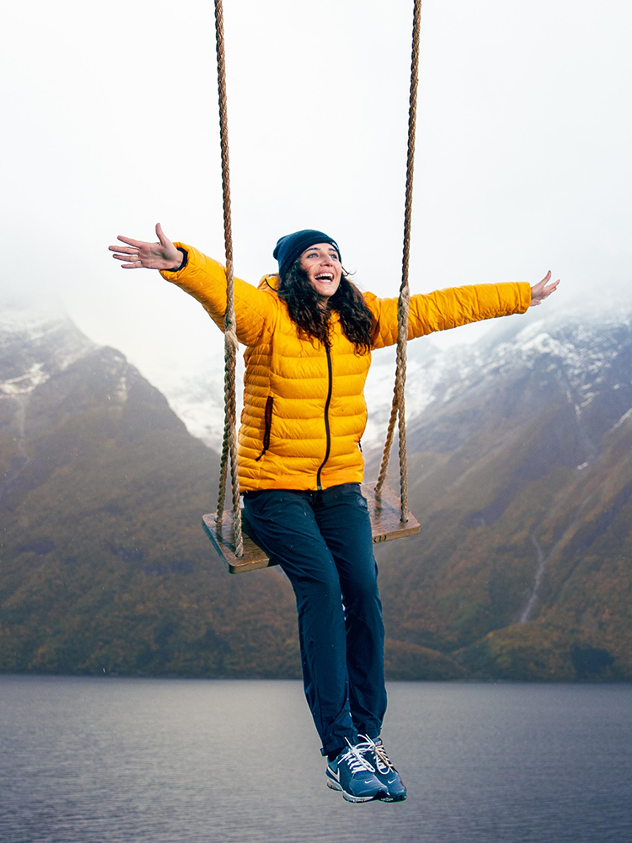Una persona in altalena con vista sulle montagne innevate e sullo Hjørundfjord nella Norvegia dei fiordi