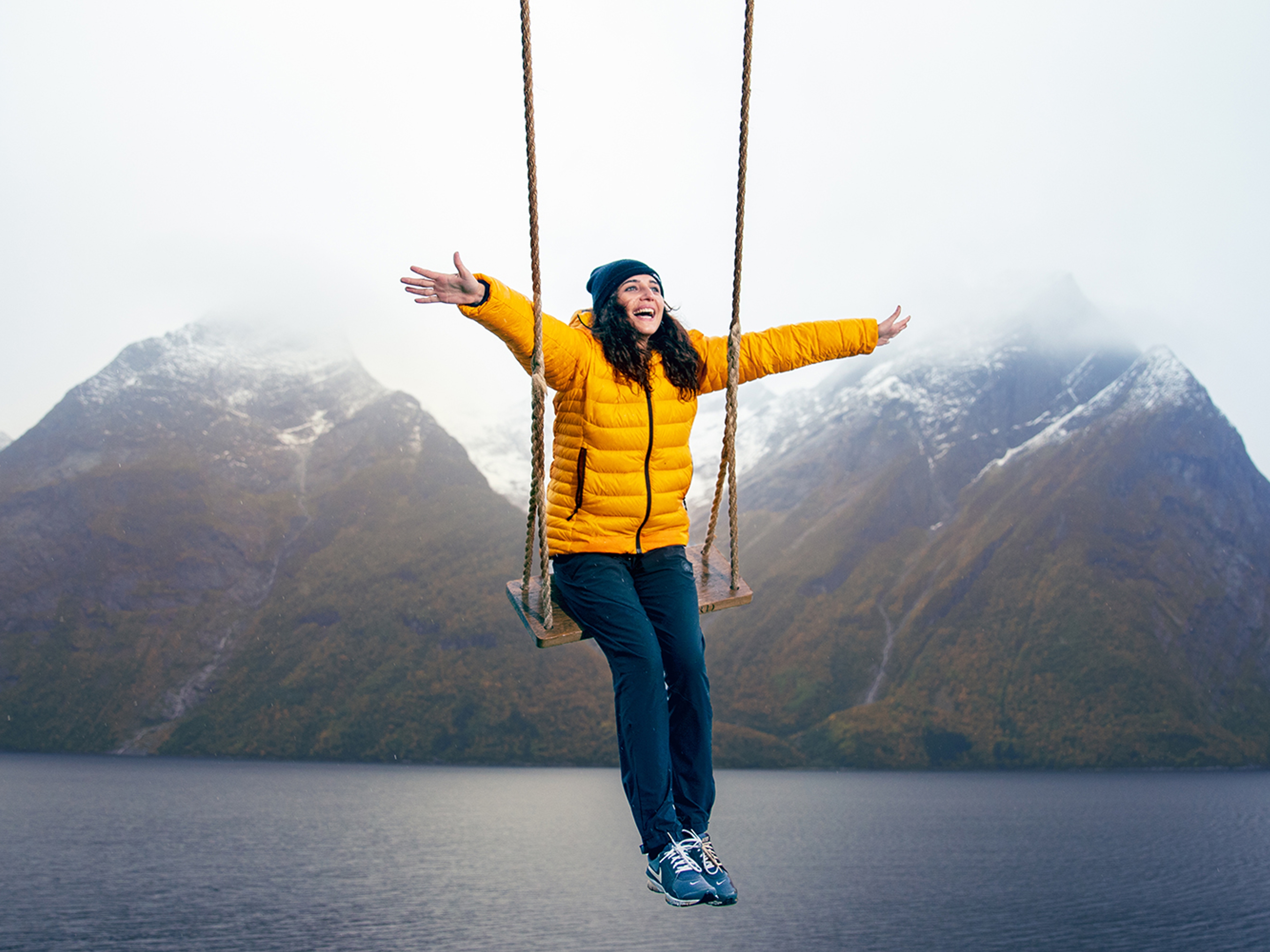 A person on a swing with views of snow-clad mountains and the Hjørundfjord in Fjord Norway