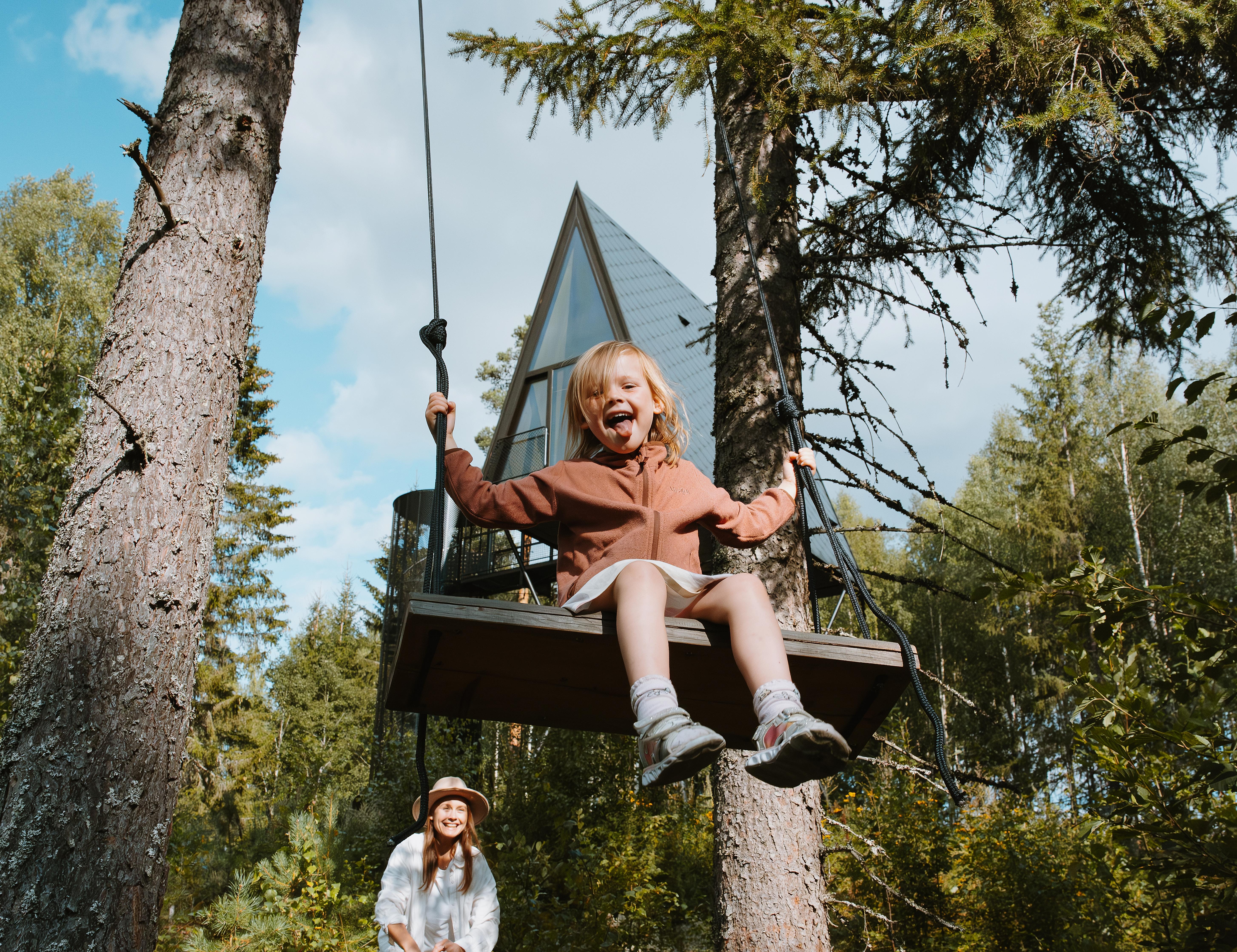 A girl is smiling on a swing in front of a treetop cabin