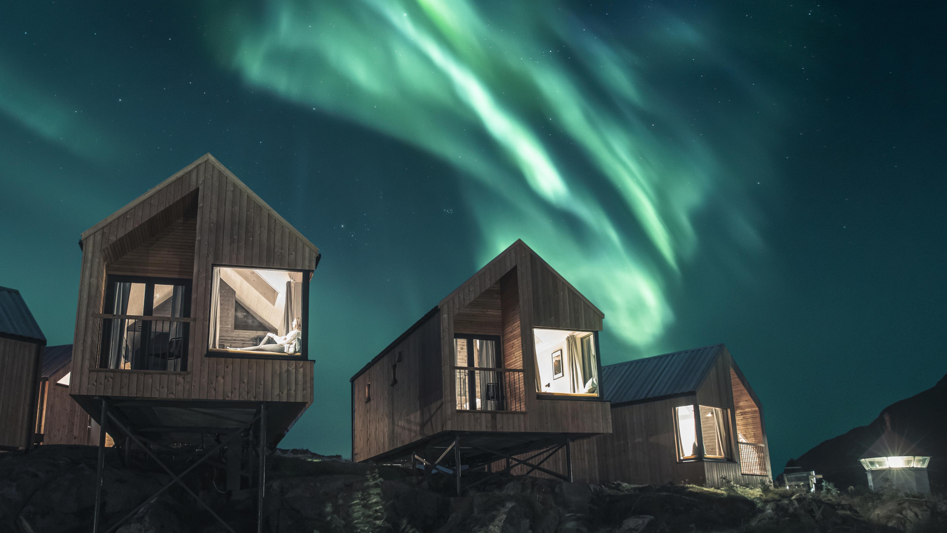 Person chilling in one of the cabins at Hattvika Lodge, with Northern Lights dancing on the sky