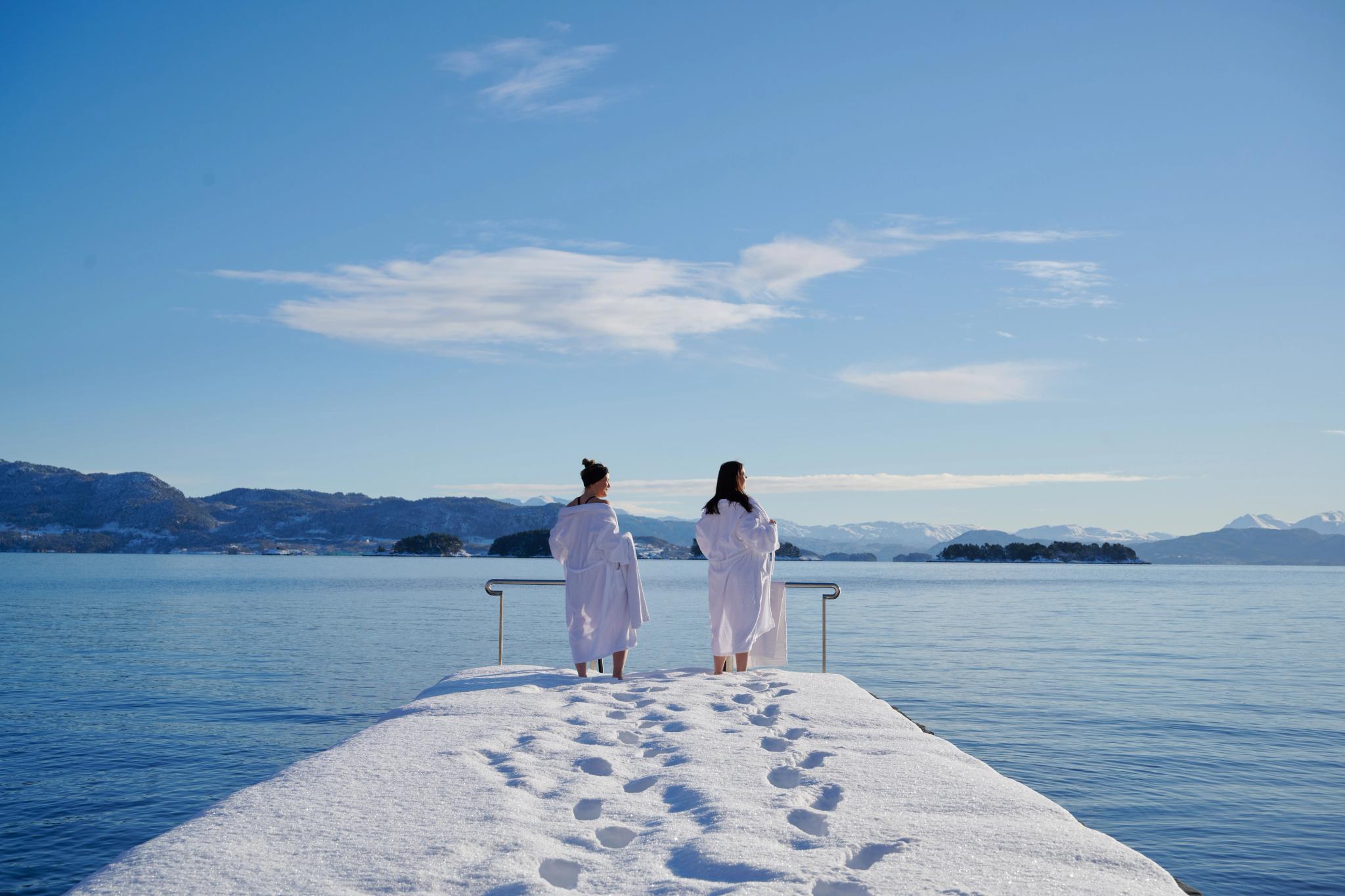 Two people standing by the fjord at Soldtrand Hotel & Bad in winter, Norway.